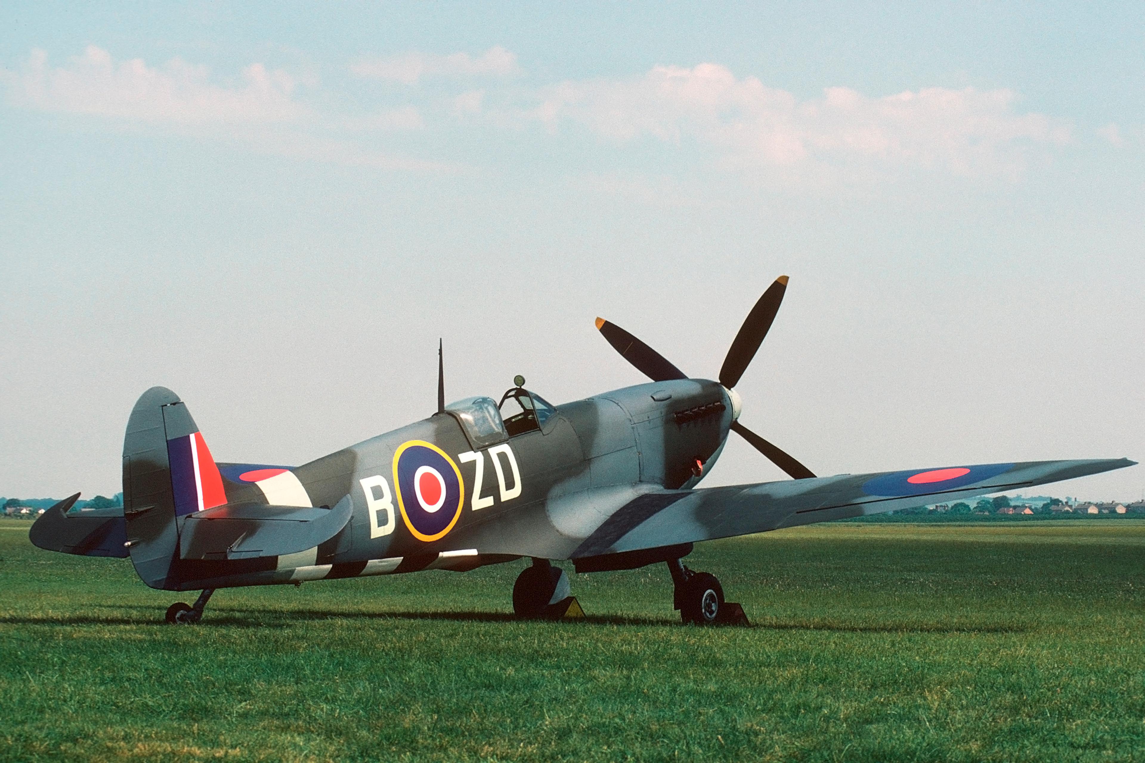 A vintage World War II-era fighter plane, with British roundel markings, parked on a grassy field under a clear sky.