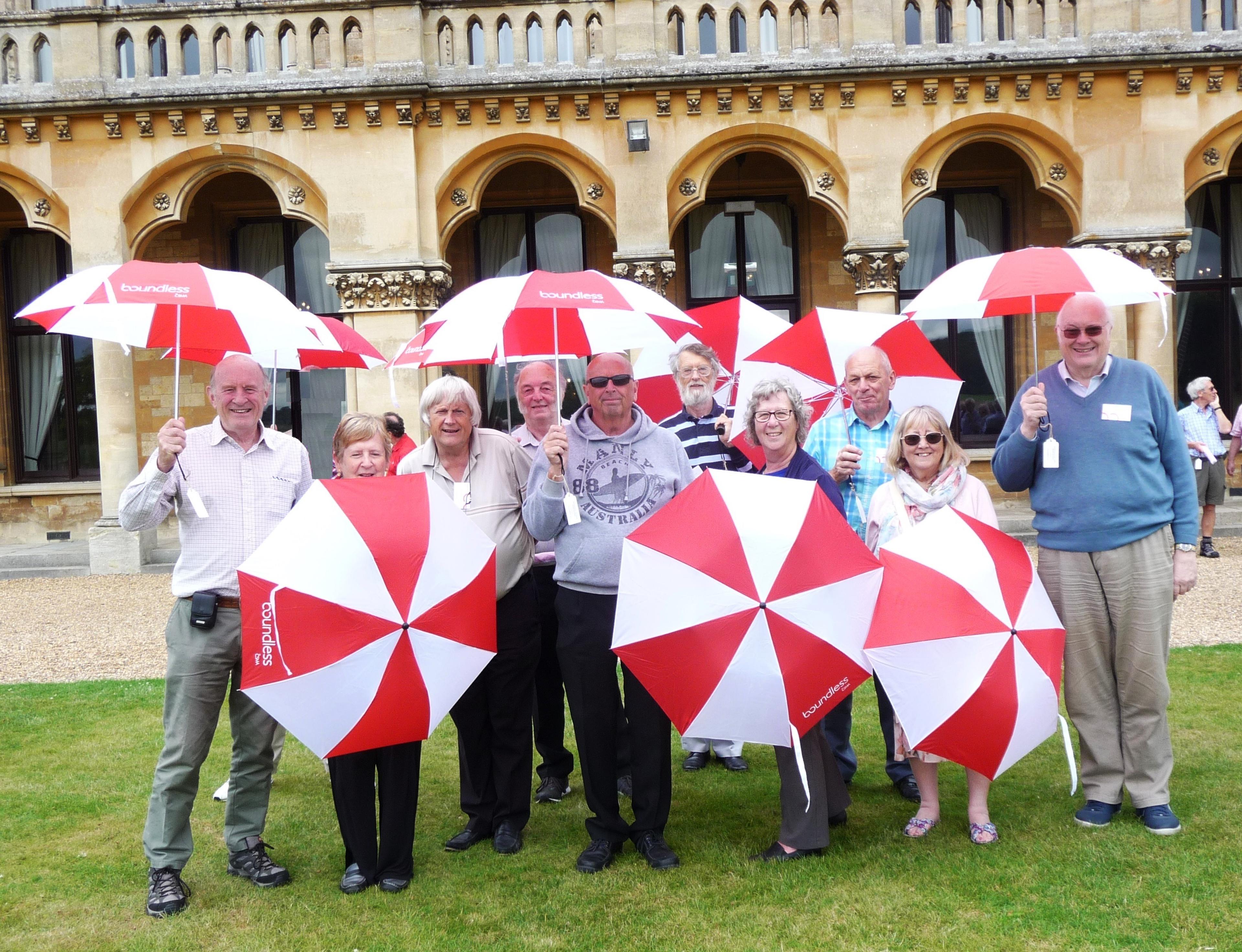 A group of people stands in front of a historic building, smiling and holding Boundless umbrellas