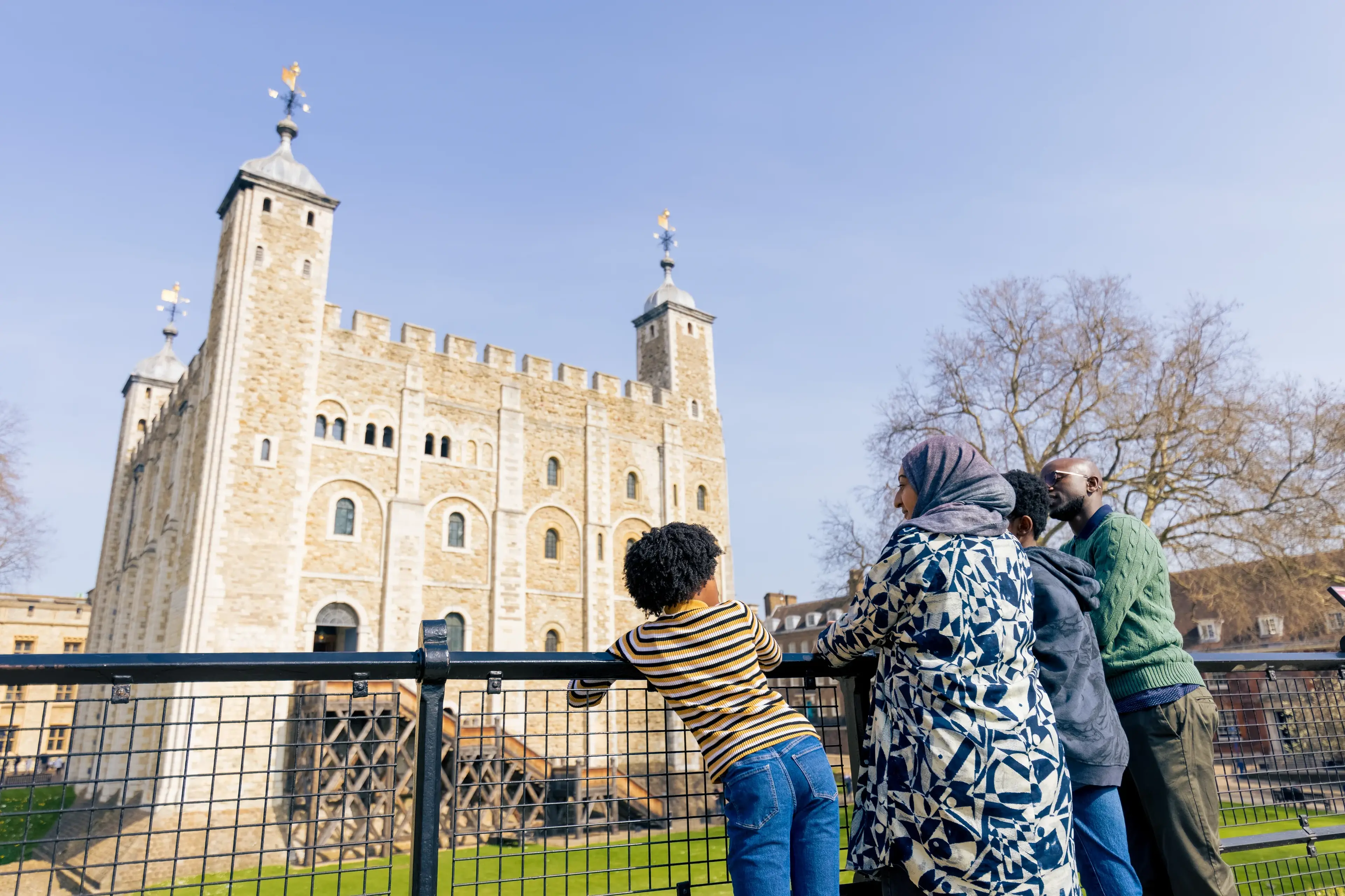 A group of people, including a child, admire the historic stone architecture of the Tower of London on a clear day.
