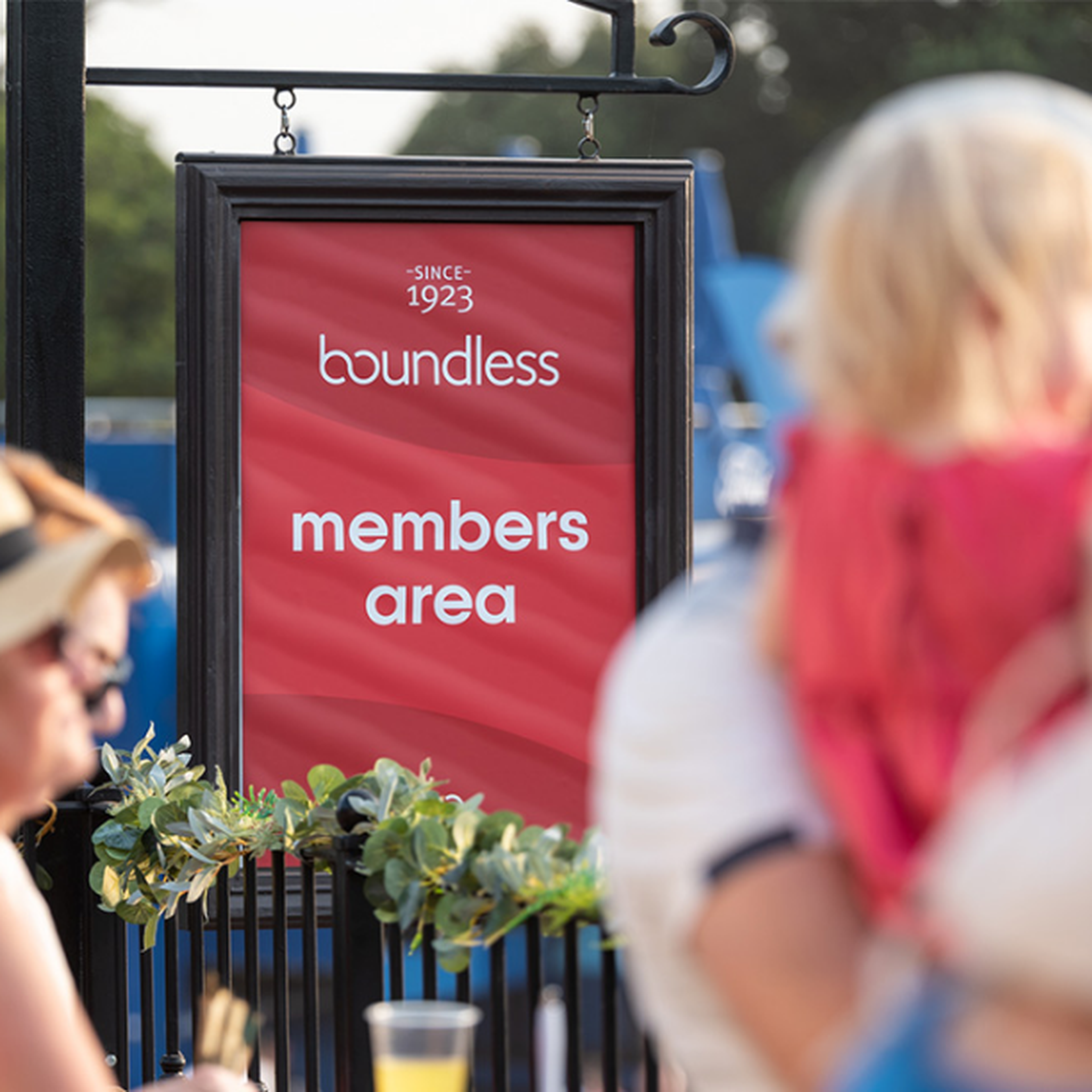 Sign reading "boundless members area" in a red frame hangs outdoors, surrounded by blurred people in casual attire.