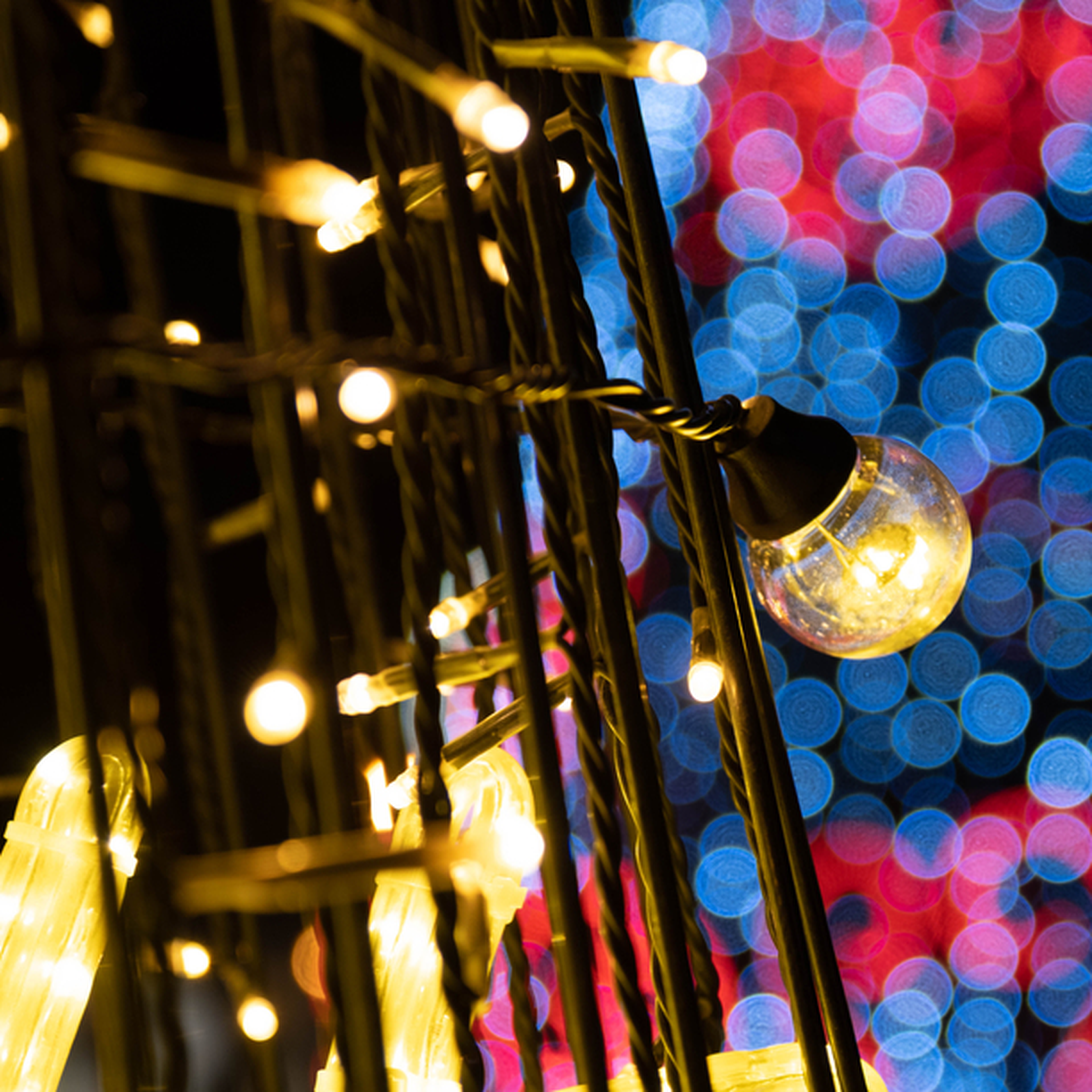 Close-up of glowing string lights with a blurred background of red and blue bokeh, creating a festive atmosphere.