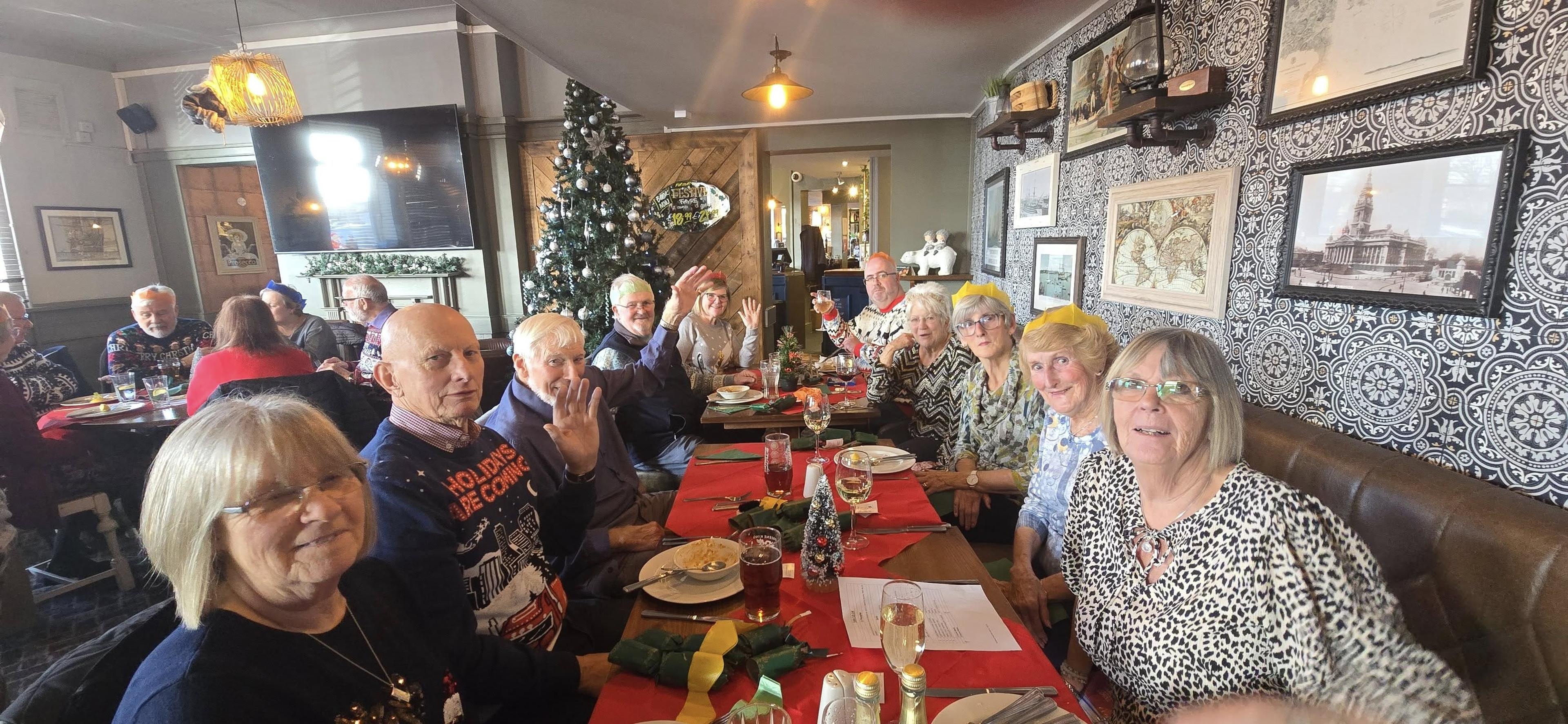 A group of people enjoying a festive meal in a decorated restaurant with a Christmas tree