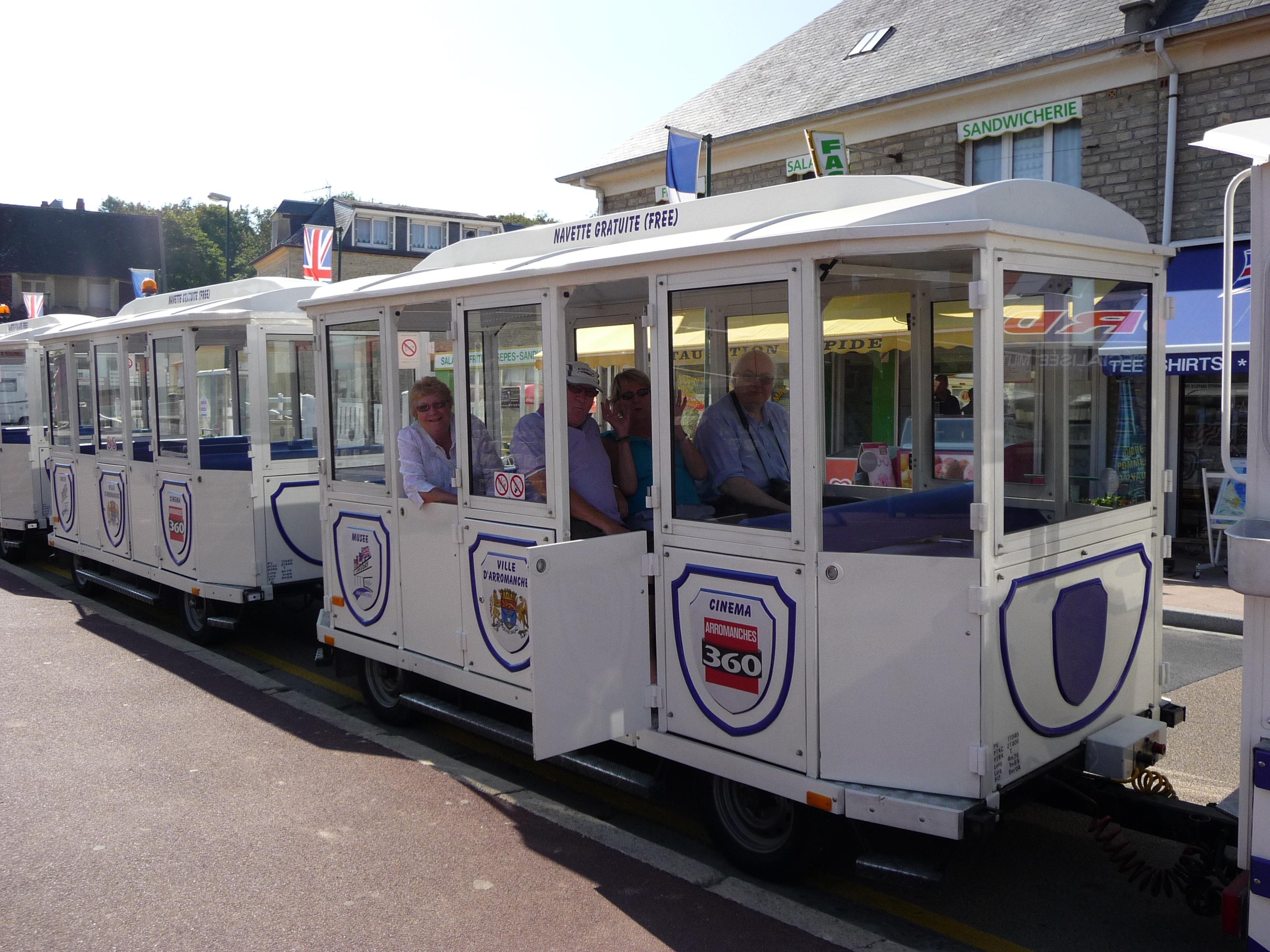 White tourist train with seated passengers in a sunny street