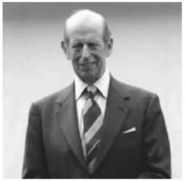 Elderly man in a suit and striped tie, standing against a plain background.