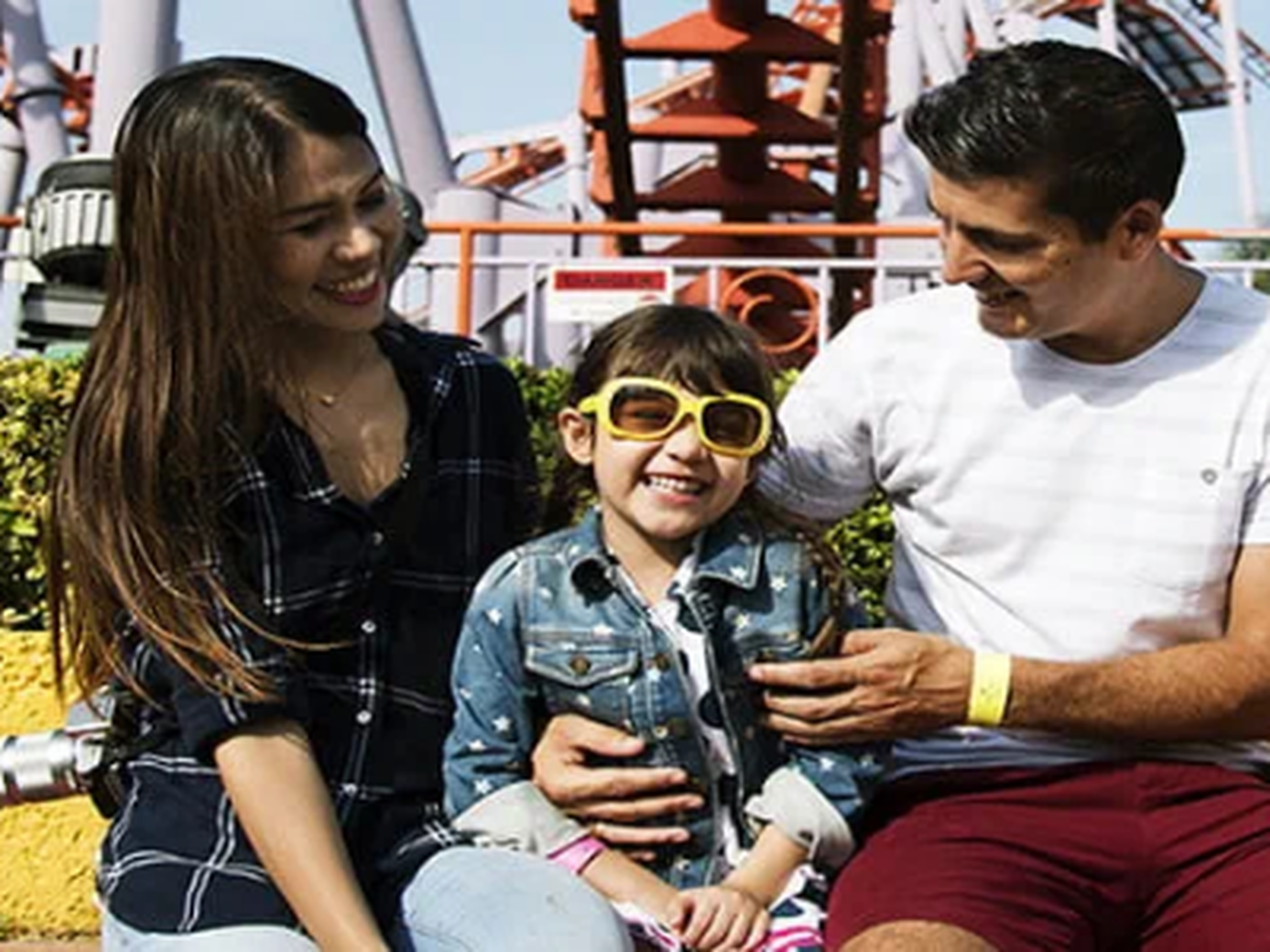 Child with sunglasses and family sitting in front of a rollercoaster