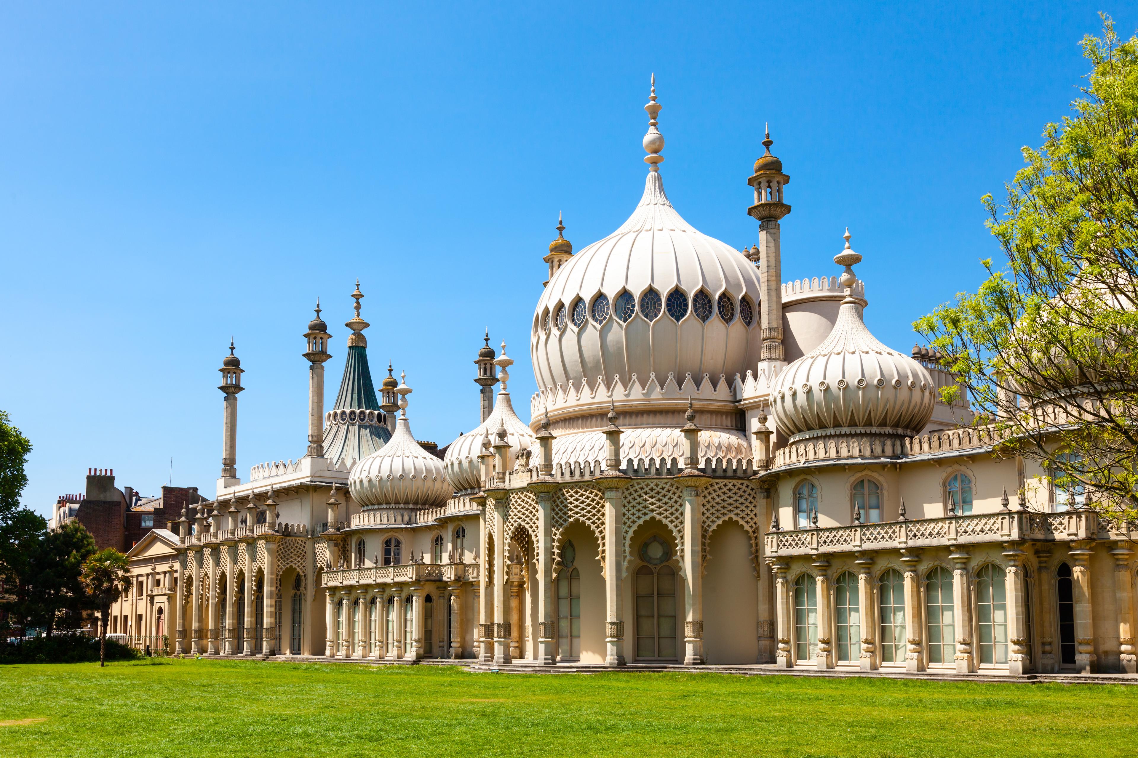 The Royal Pavilion in Brighton, England, with onion-shaped domes and ornate architecture, set against a clear blue sky and green lawn.