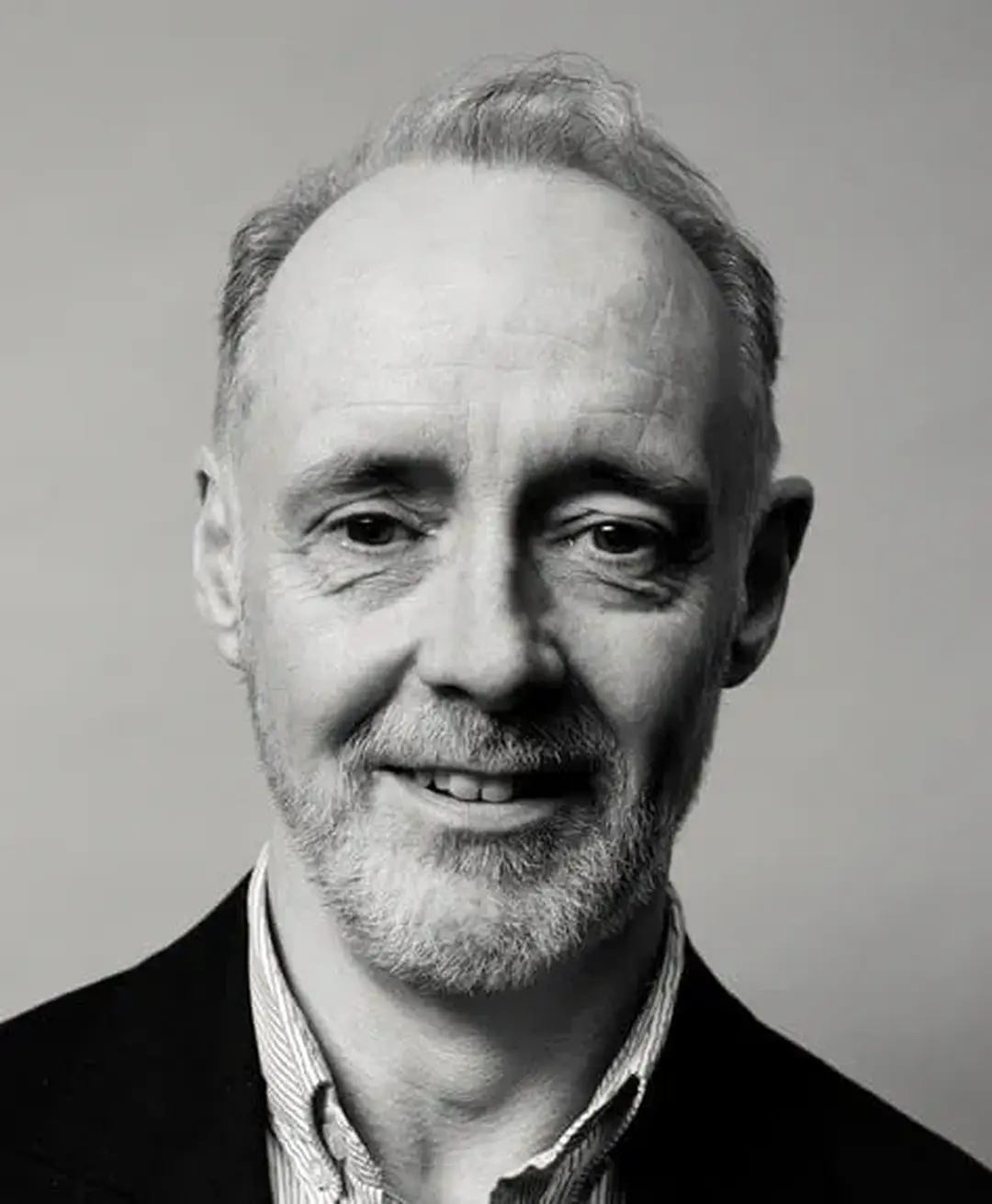 Black and white photo of a middle-aged man with a beard and short hair, smiling slightly, wearing a collared shirt and jacket.