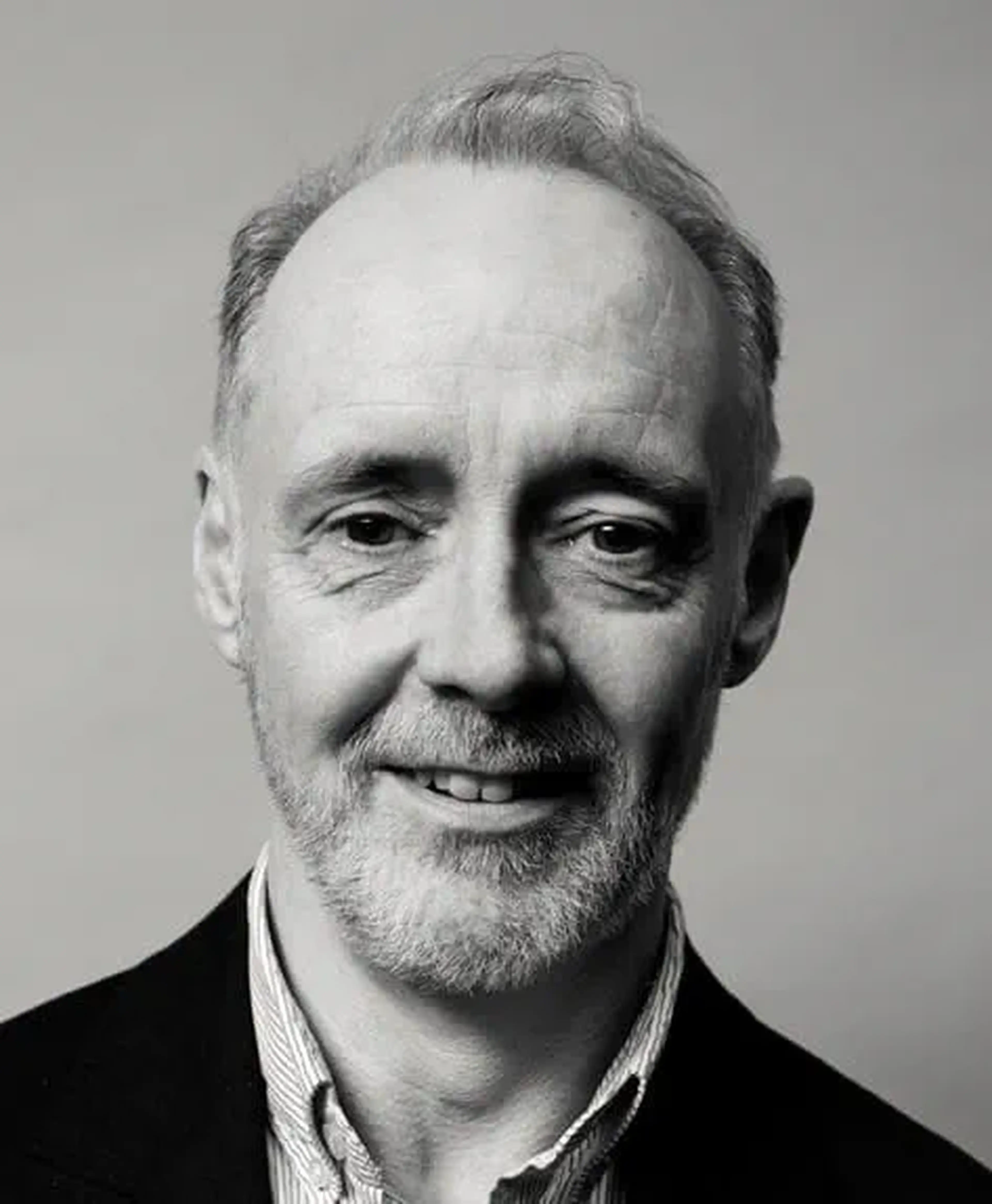 Black and white photo of a middle-aged man with a beard and short hair, smiling slightly, wearing a collared shirt and jacket.