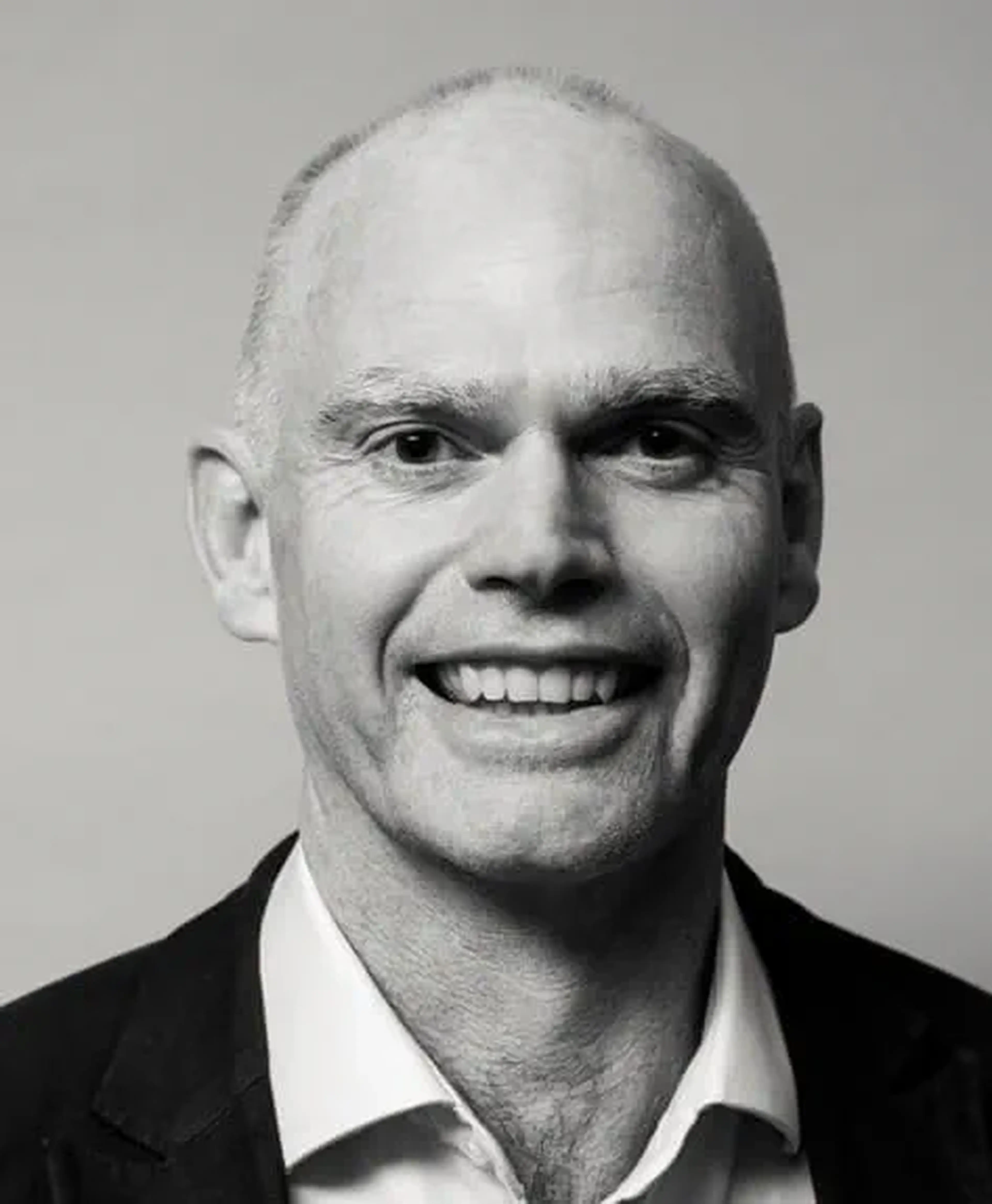 Smiling bald man in a suit and dress shirt, photographed against a plain background.