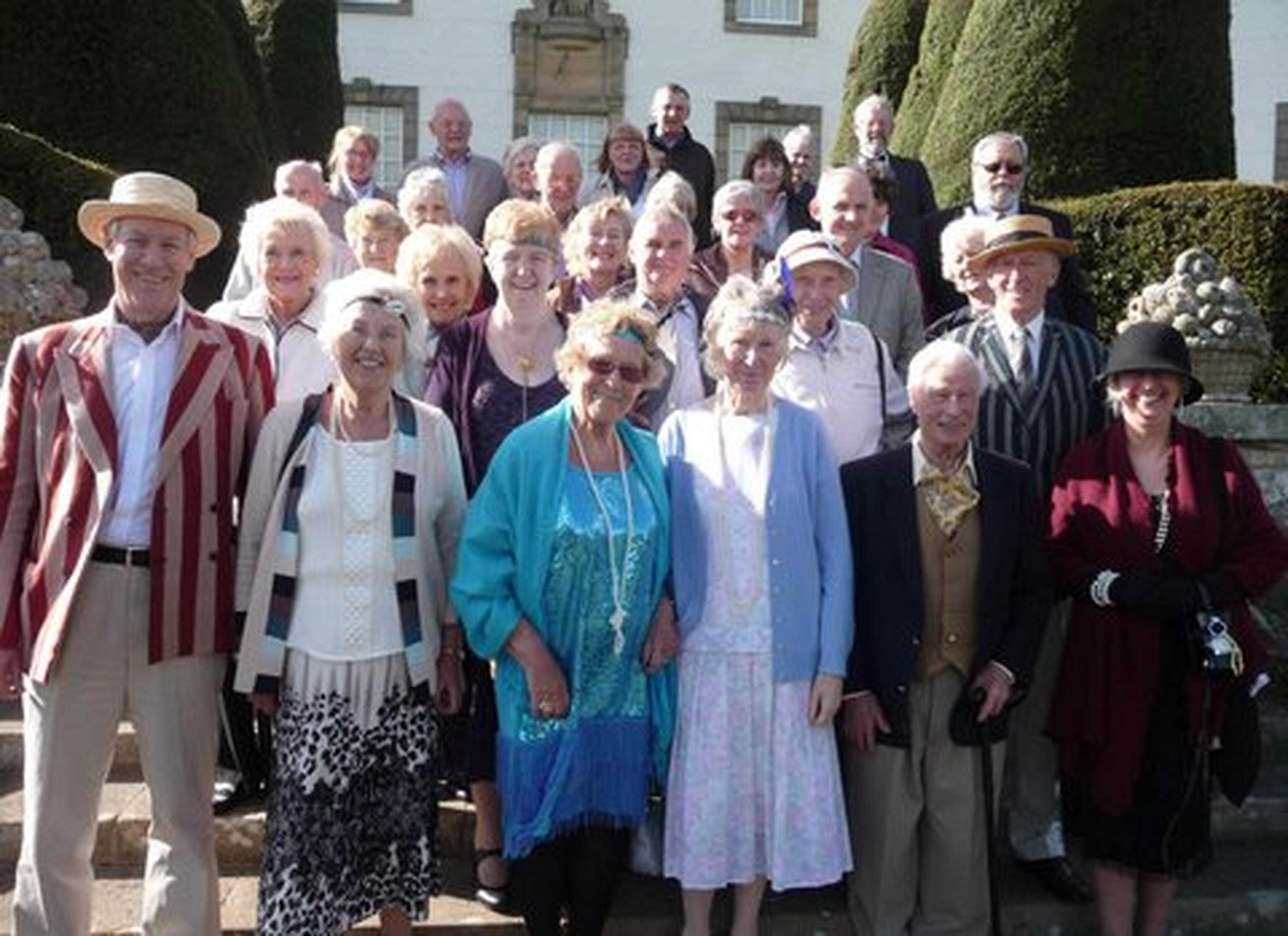Group of smiling people in vintage attire pose on outdoor steps