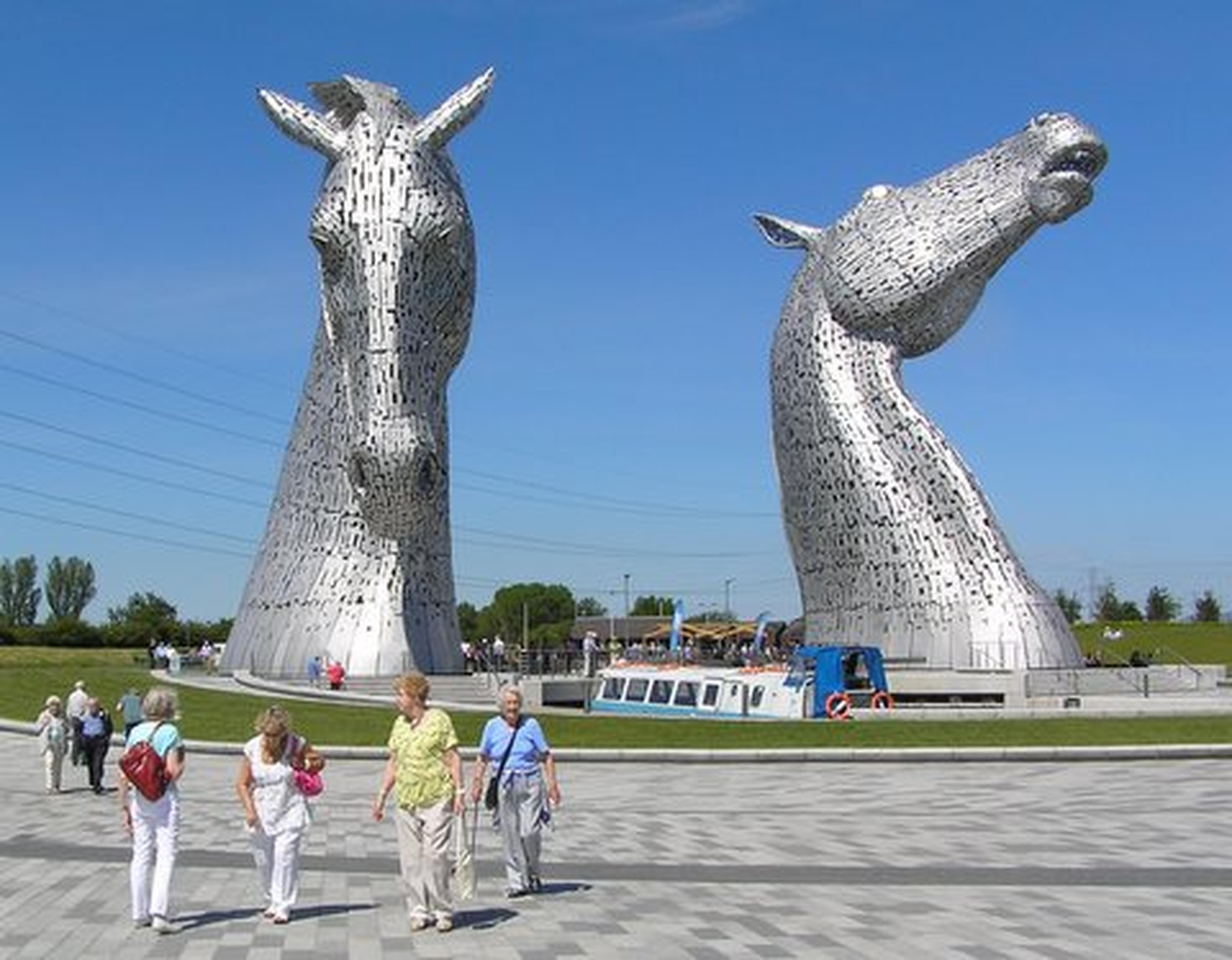 People walking past "The Kelpies"—two large horse head sculptures