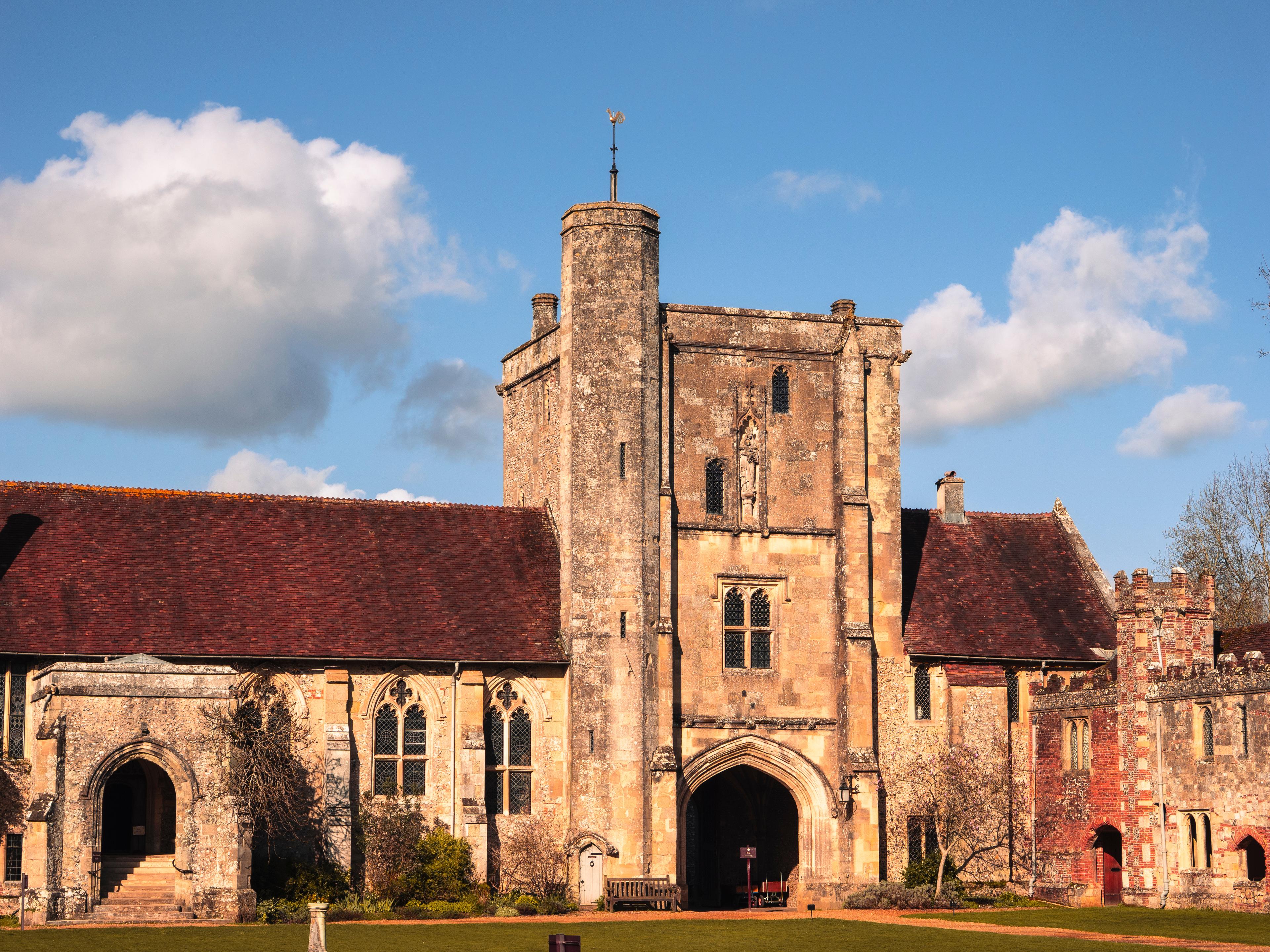 Historic stone building with a central tower, arched entrances, and sloped roofs under a bright blue sky with some clouds.