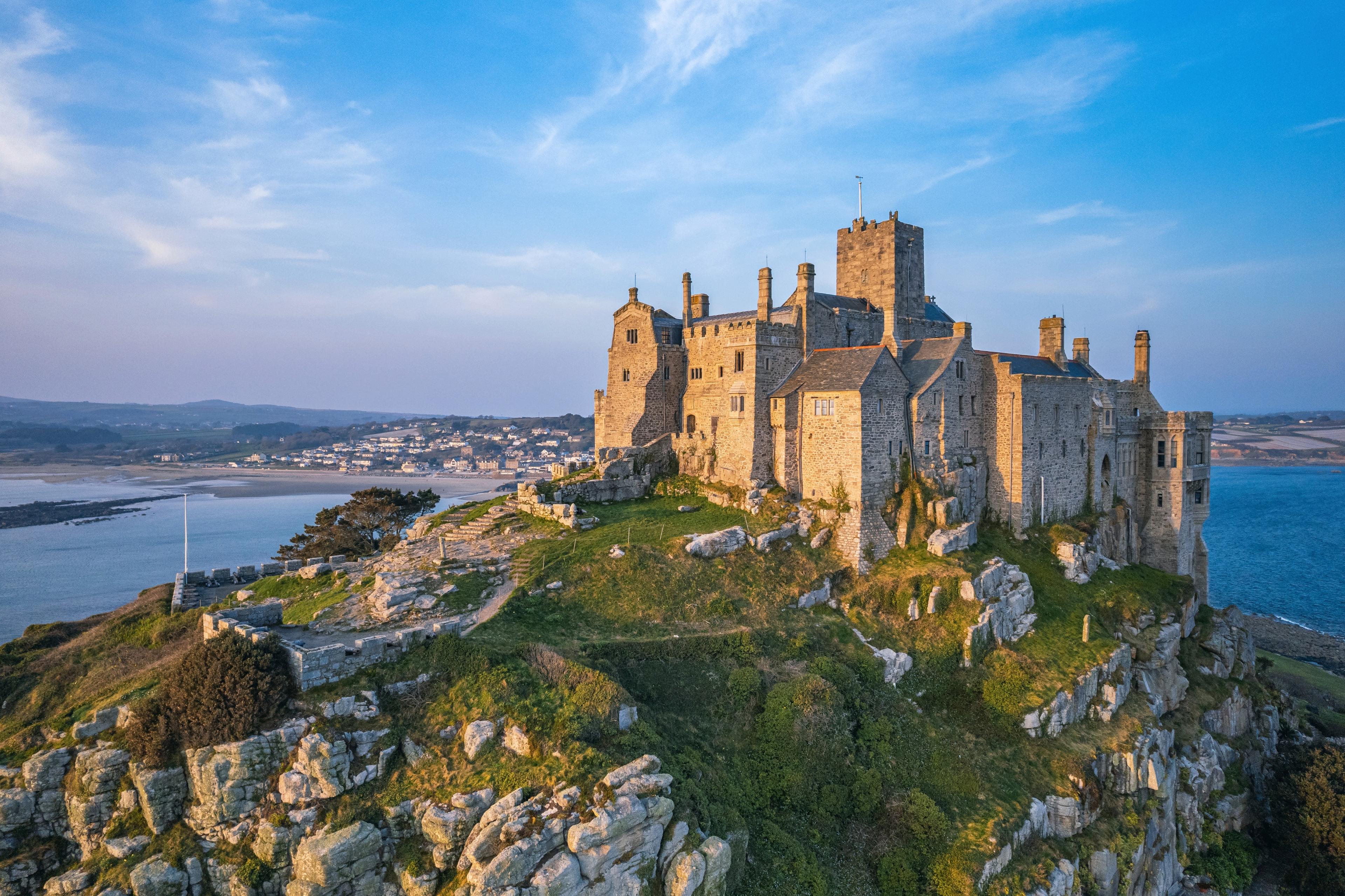 Stone castle perched on a rocky hill overlooking the sea and distant shoreline under a clear blue sky.