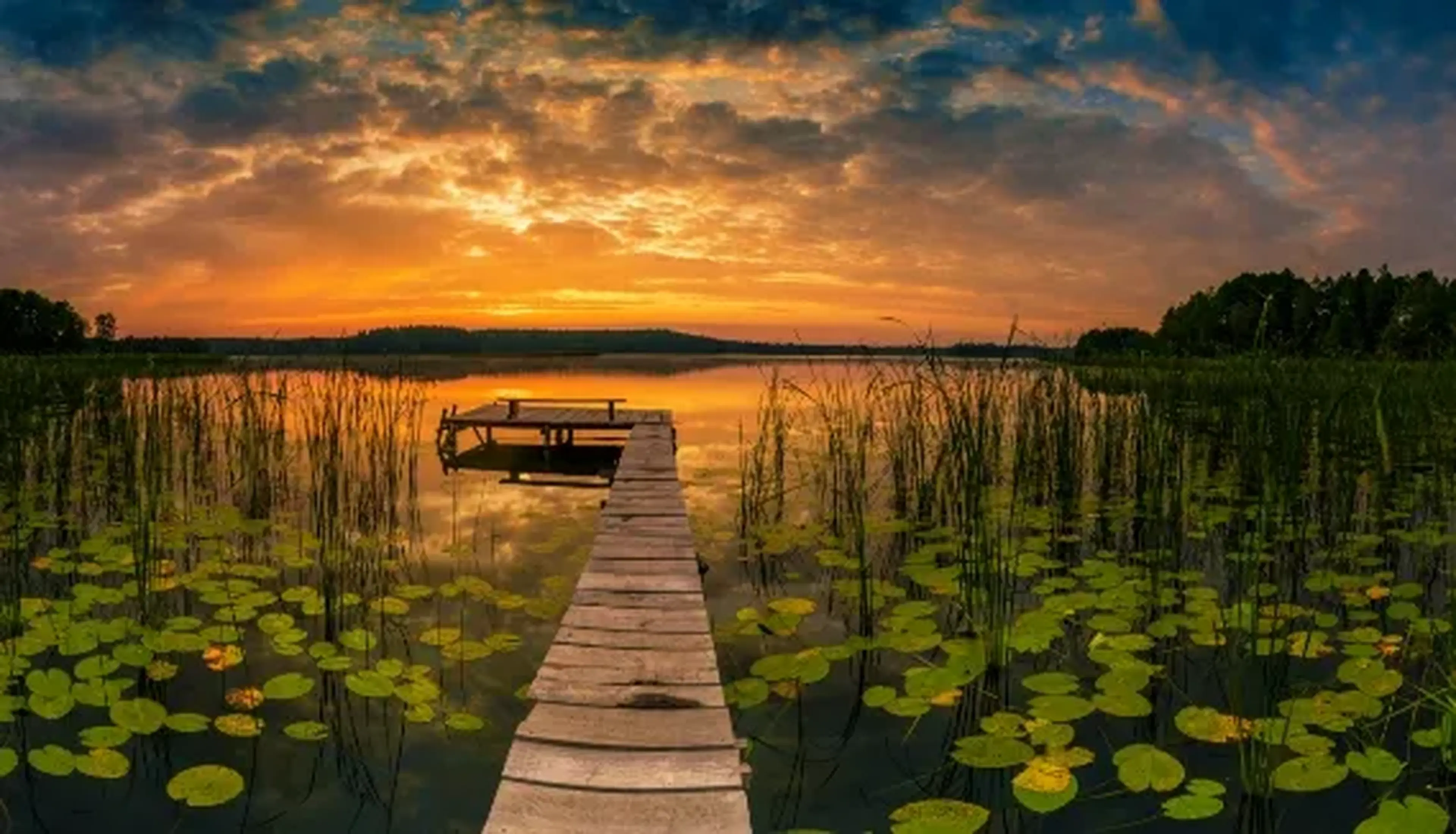 A wooden dock extends over a serene lake at sunset