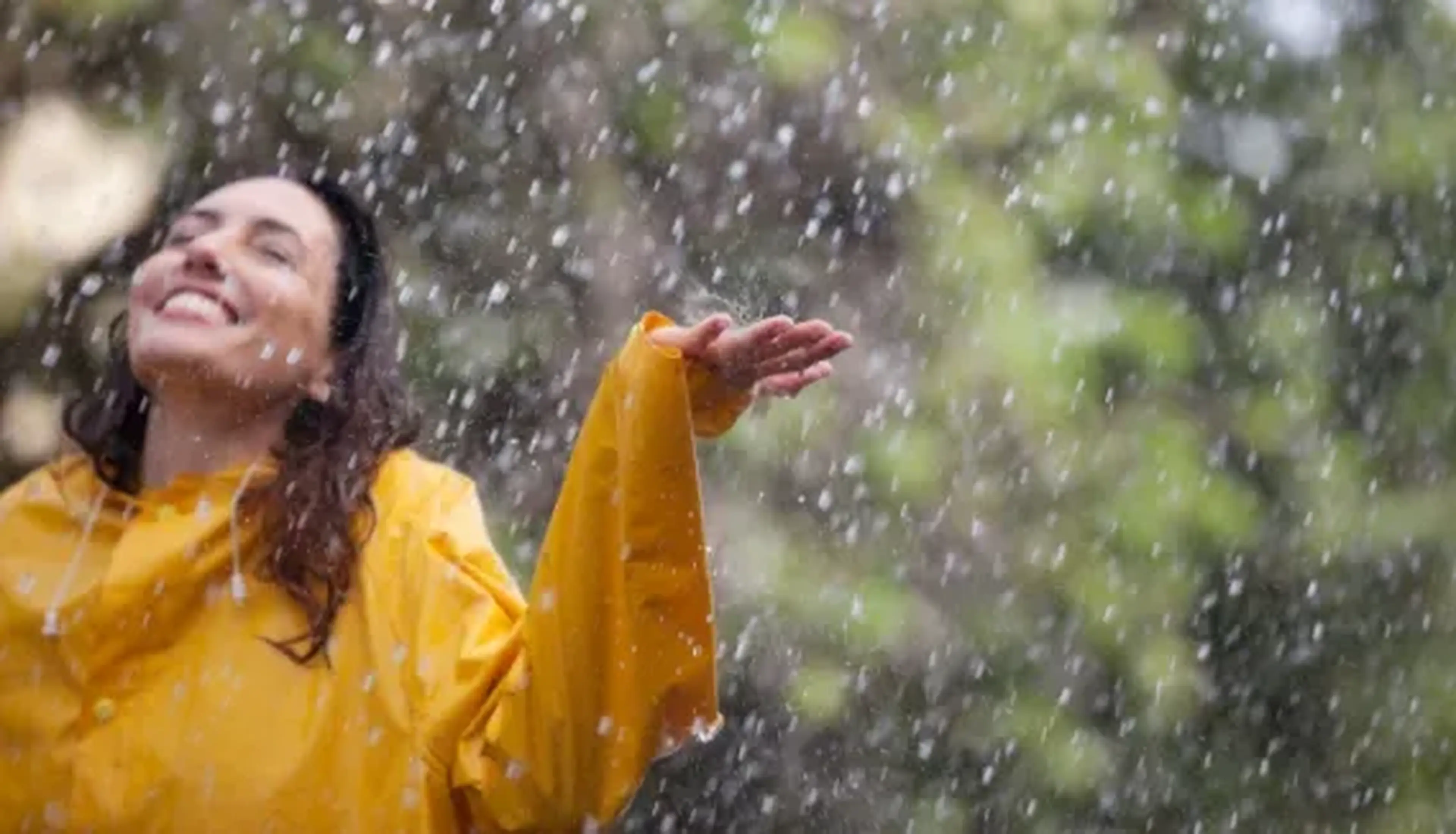 A woman in a yellow raincoat joyfully enjoying the rain