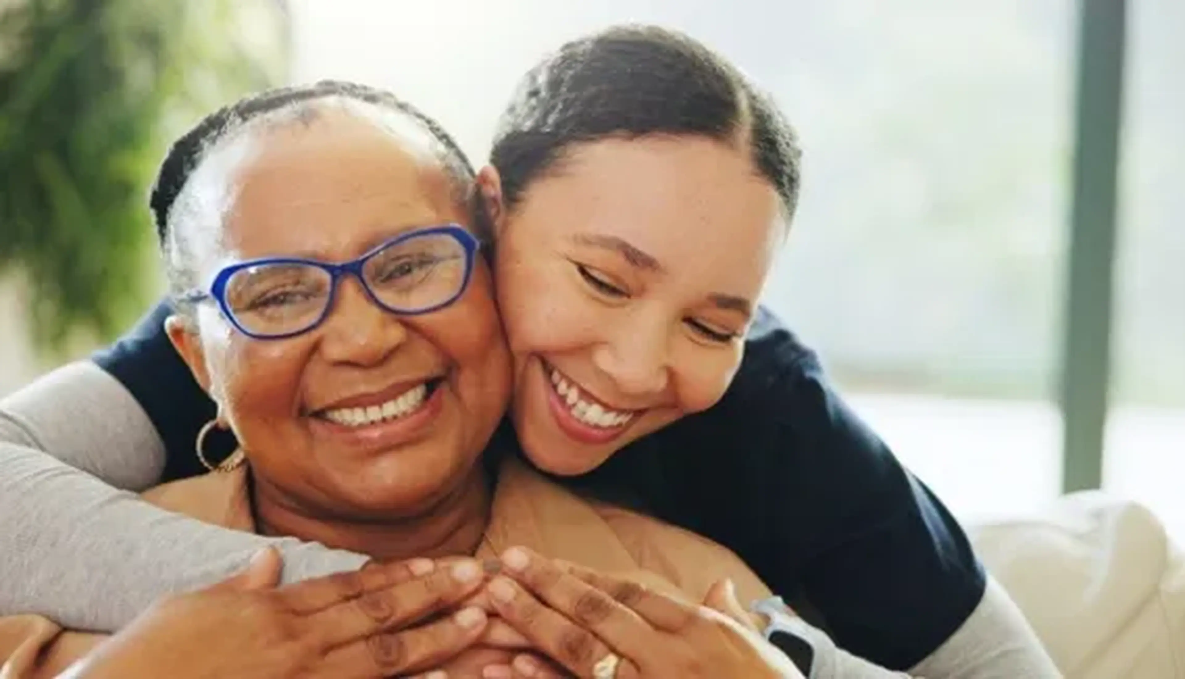 A smiling young woman embraces an older woman with glasses