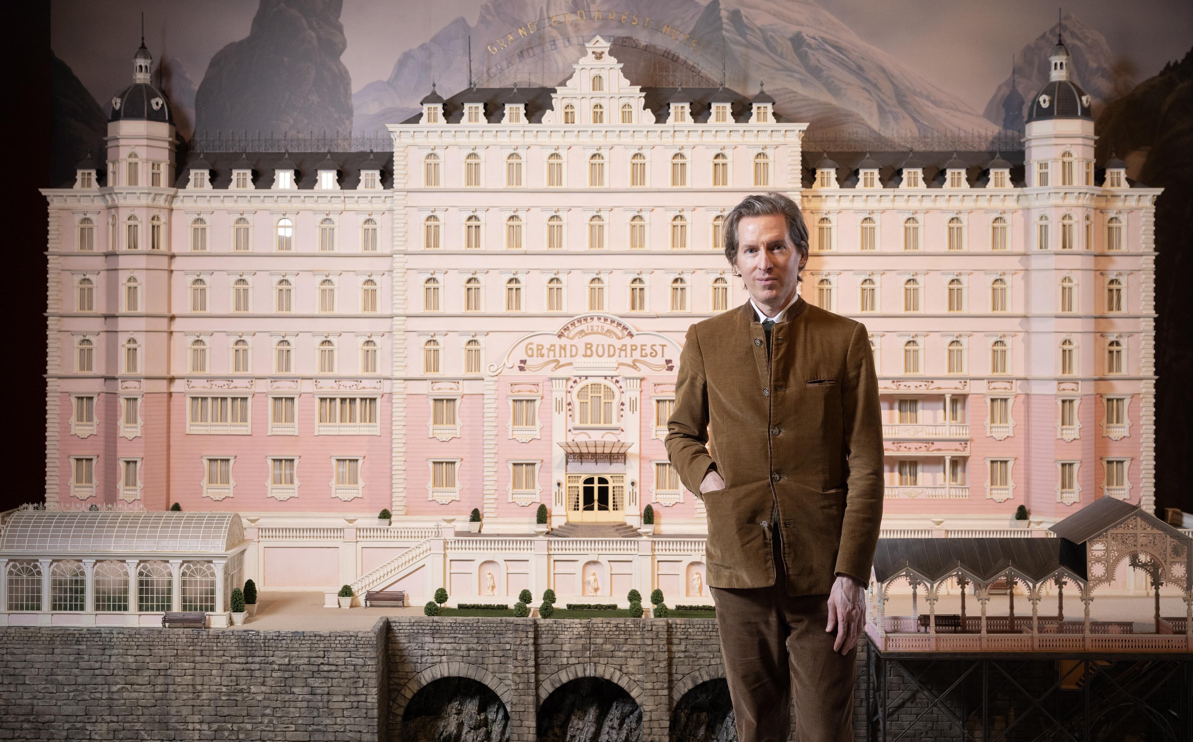 An image of wes anderson standing infront of a model of the grand budapest hotel