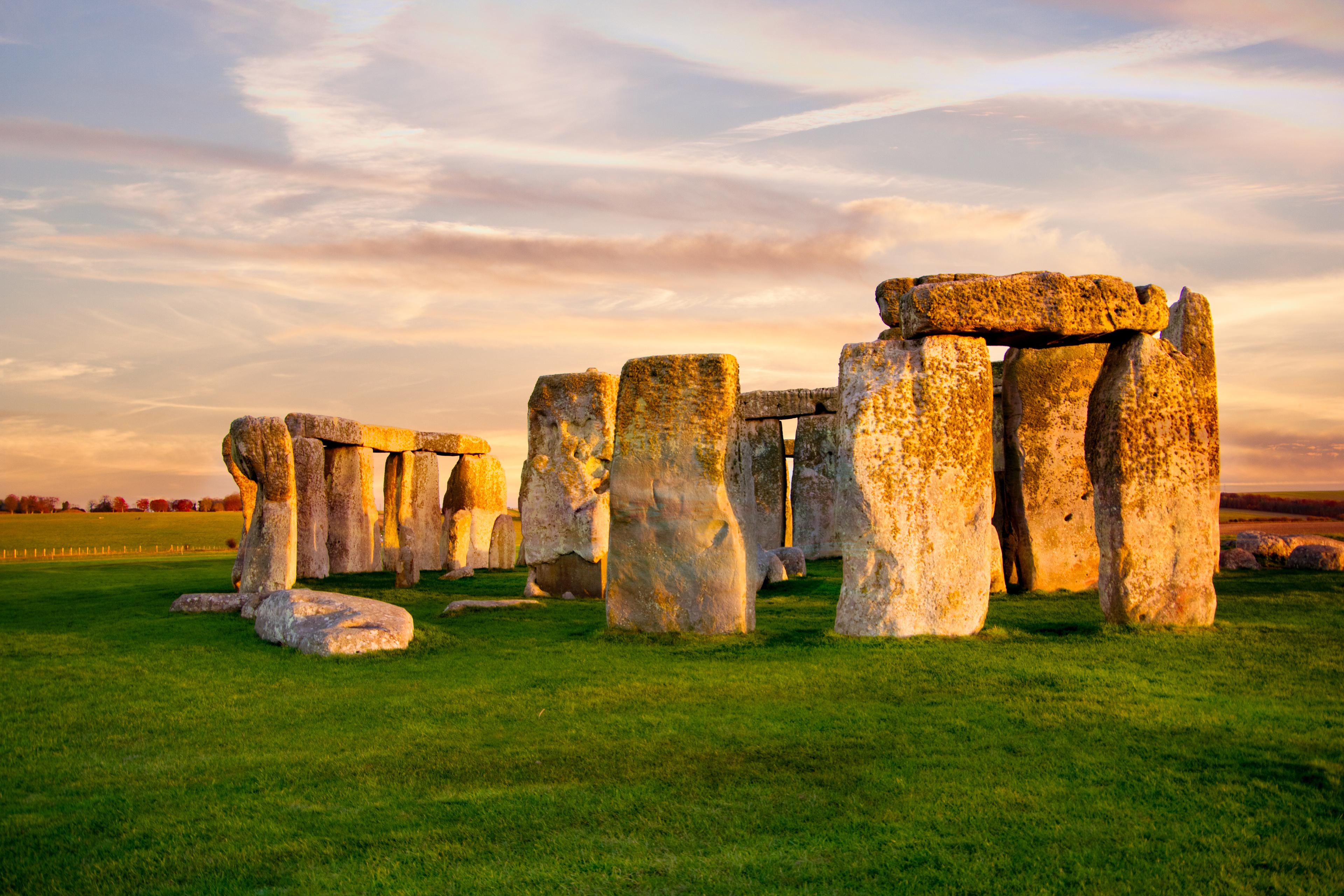 Stonehenge under a colorful sunset sky, with large stone slabs arranged upright in a circle on a grassy field.