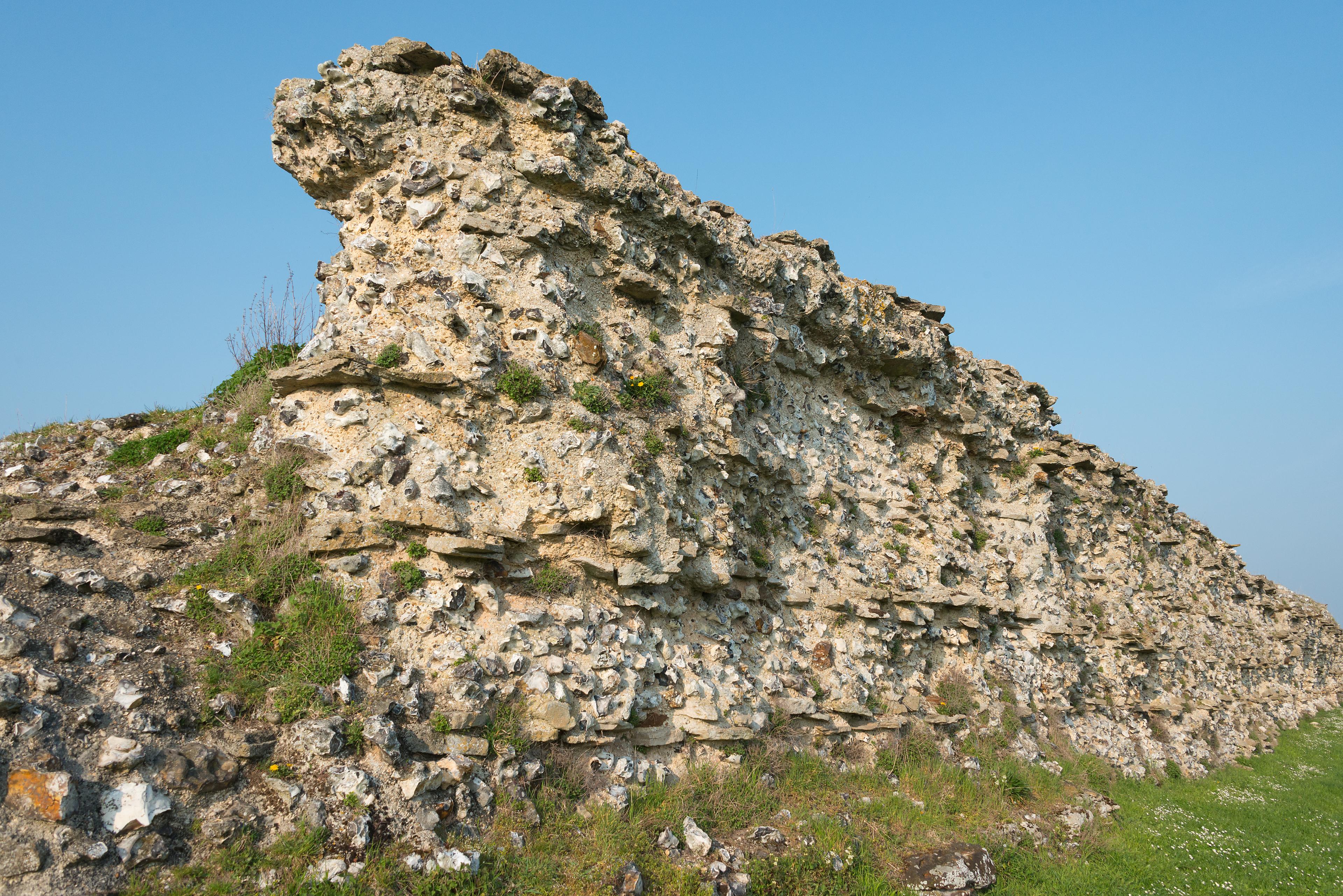 Ancient stone wall ruins against a clear blue sky, with grassy terrain at the base.