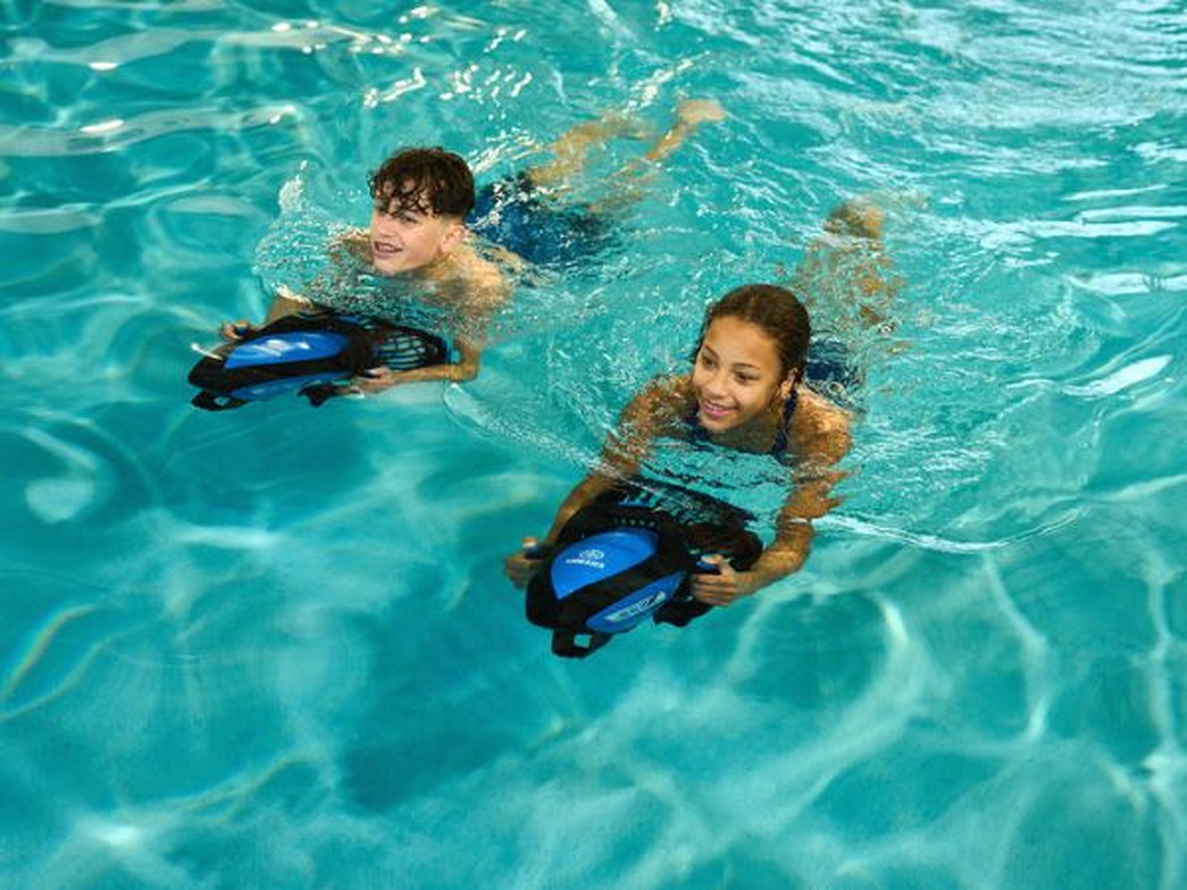 Two children swimming with underwater scooters in a clear blue pool, smiling and enjoying the water.