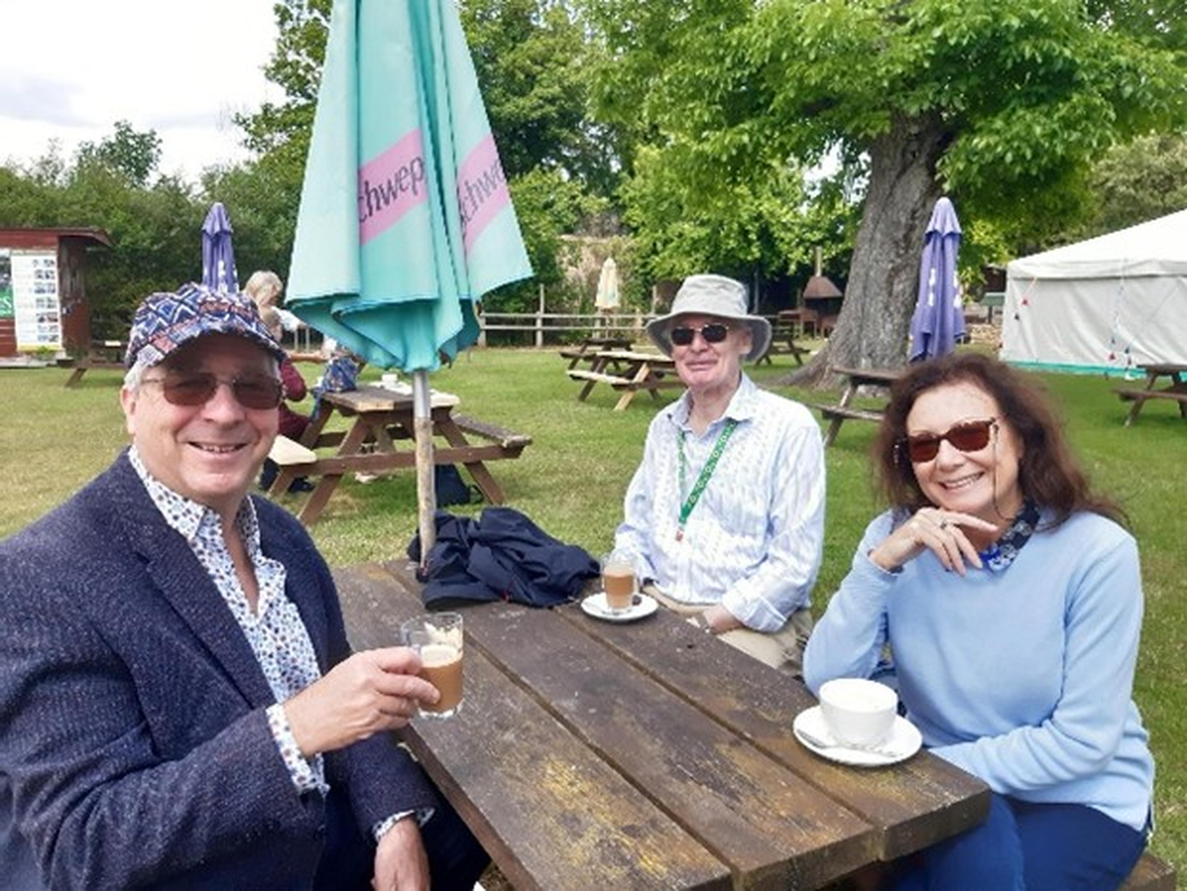 Three people sitting at an outdoor picnic table, enjoying drinks