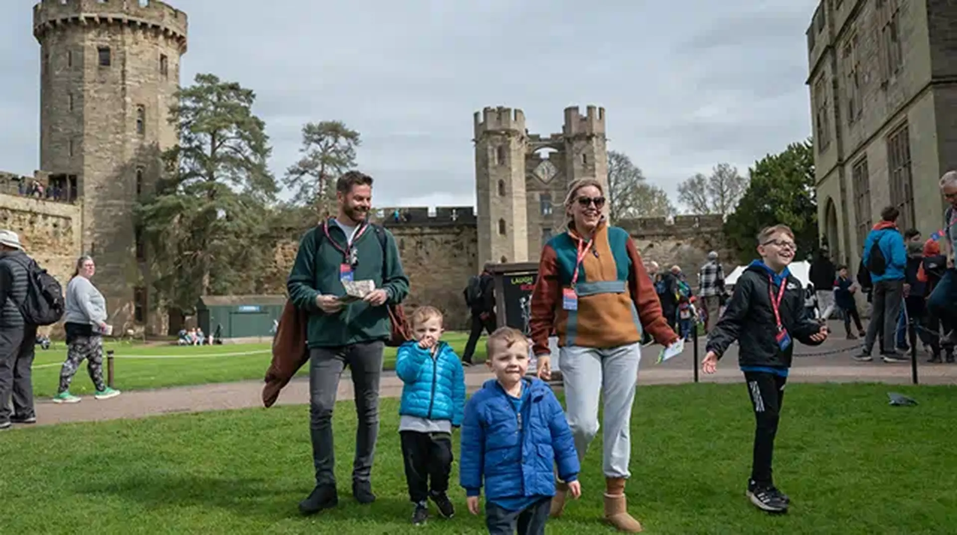 A family with three children walks on grass at a historic castle, surrounded by other visitors