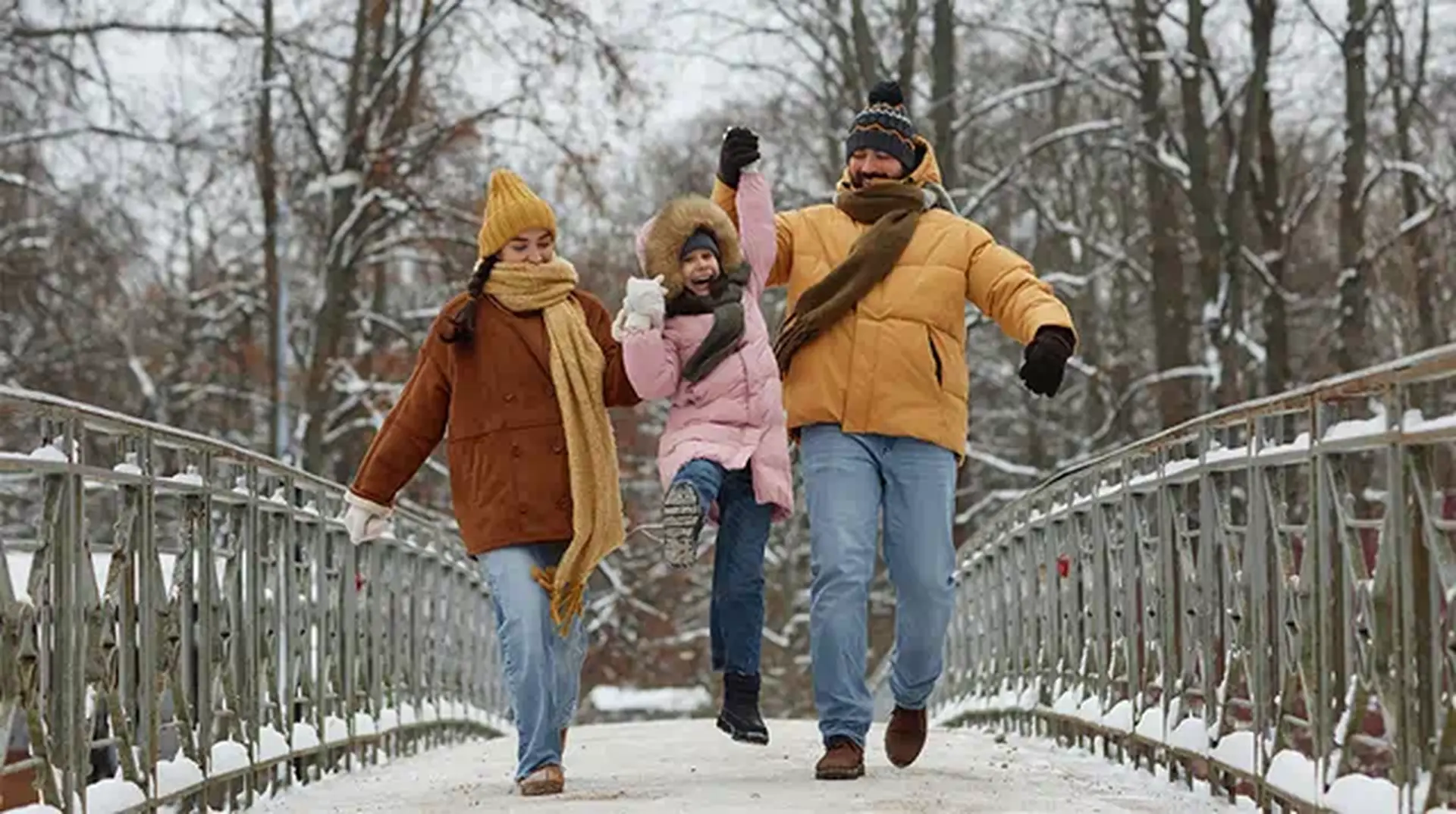 A family of three joyfully walks on a snowy bridge