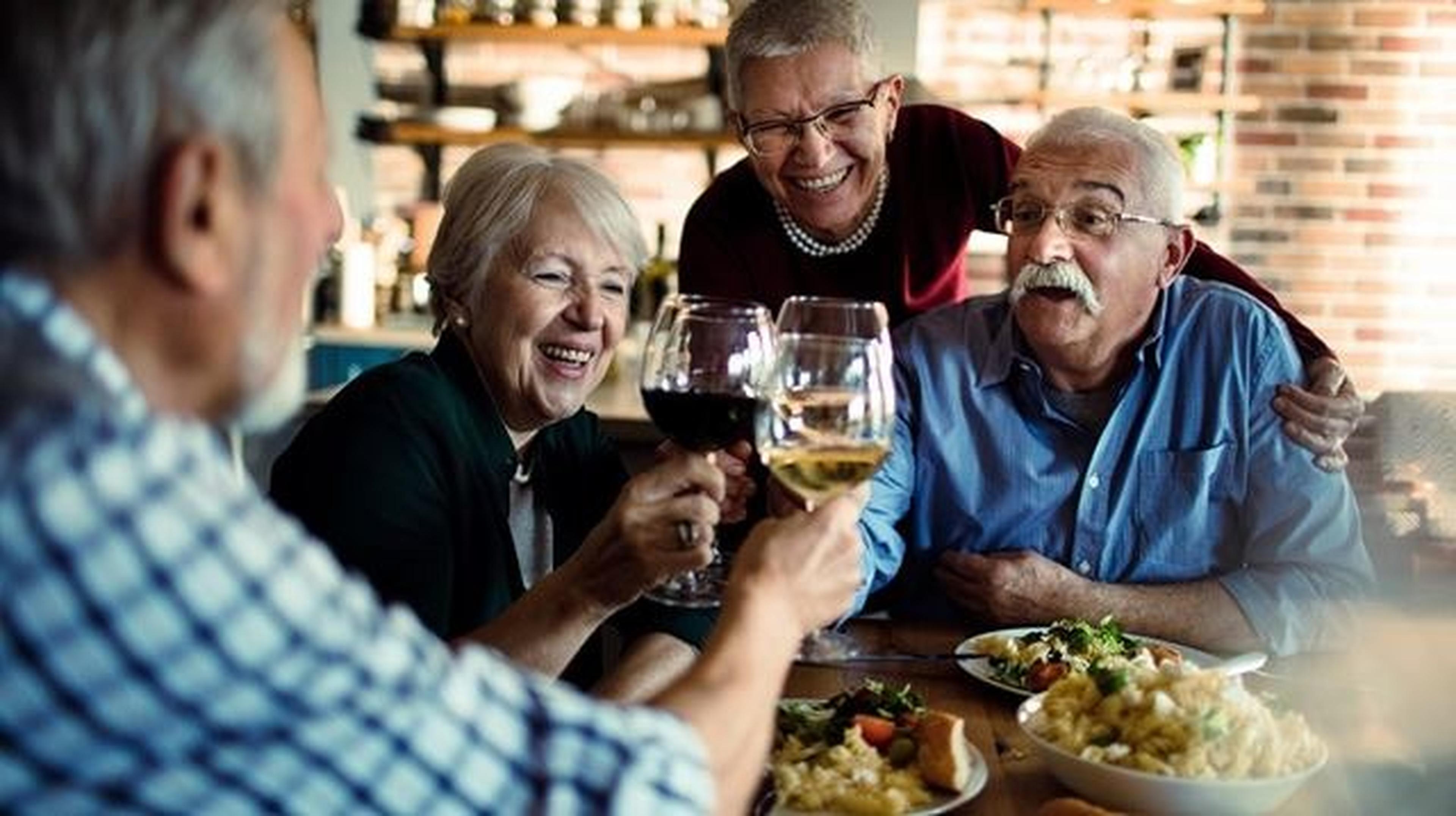 Four seniors joyfully clink wine glasses over a meal in a pub