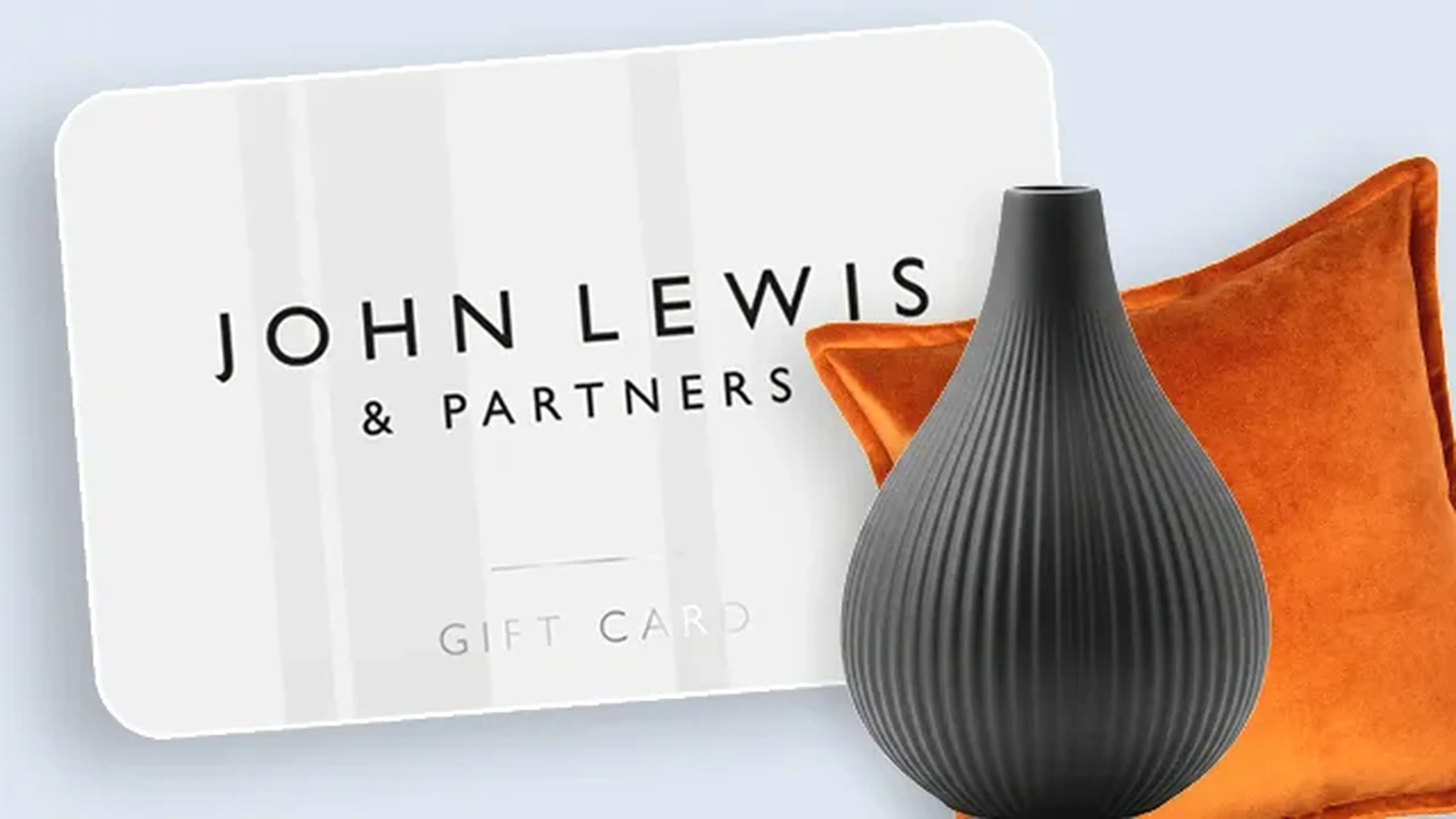 John Lewis & Partners gift card with a ridged black vase and orange velvet cushion, set against a light background.