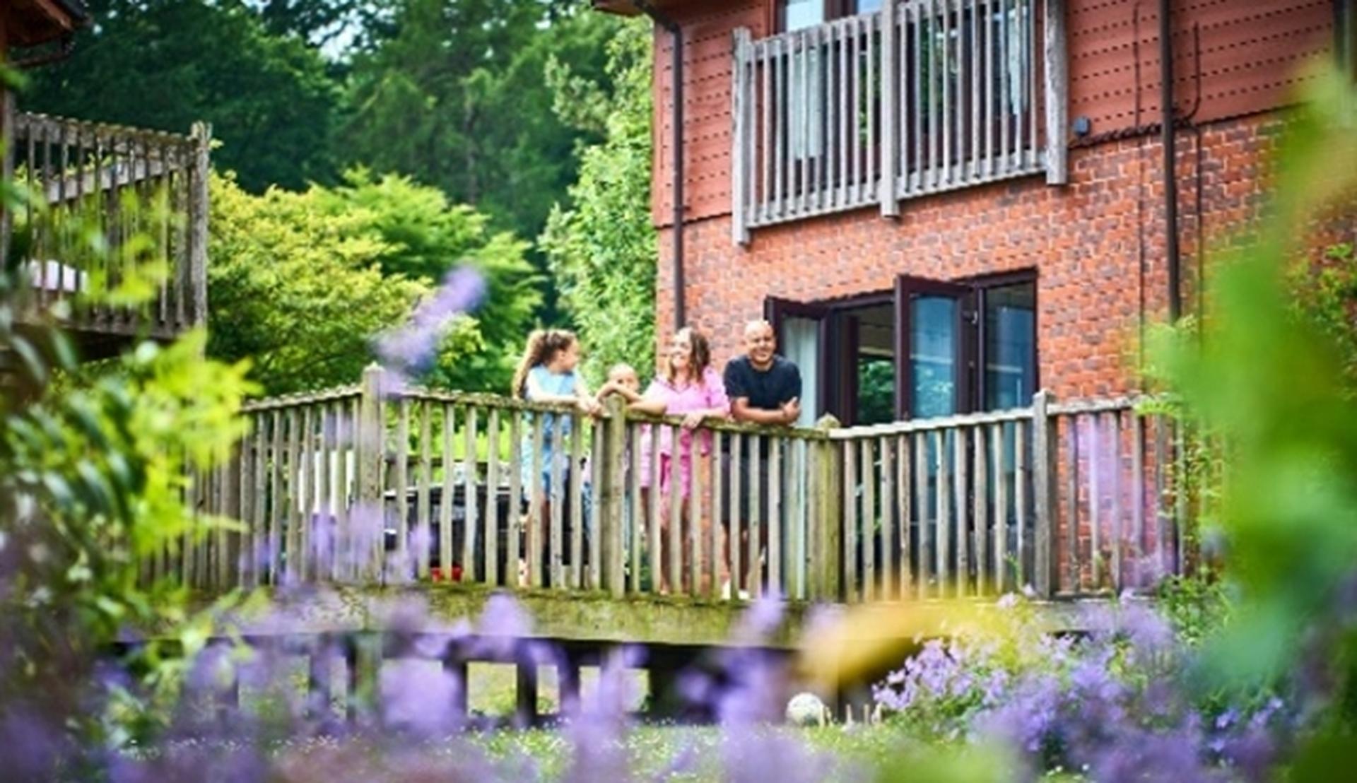 A family standing on a wooden balcony of a brick house, surrounded by greenery