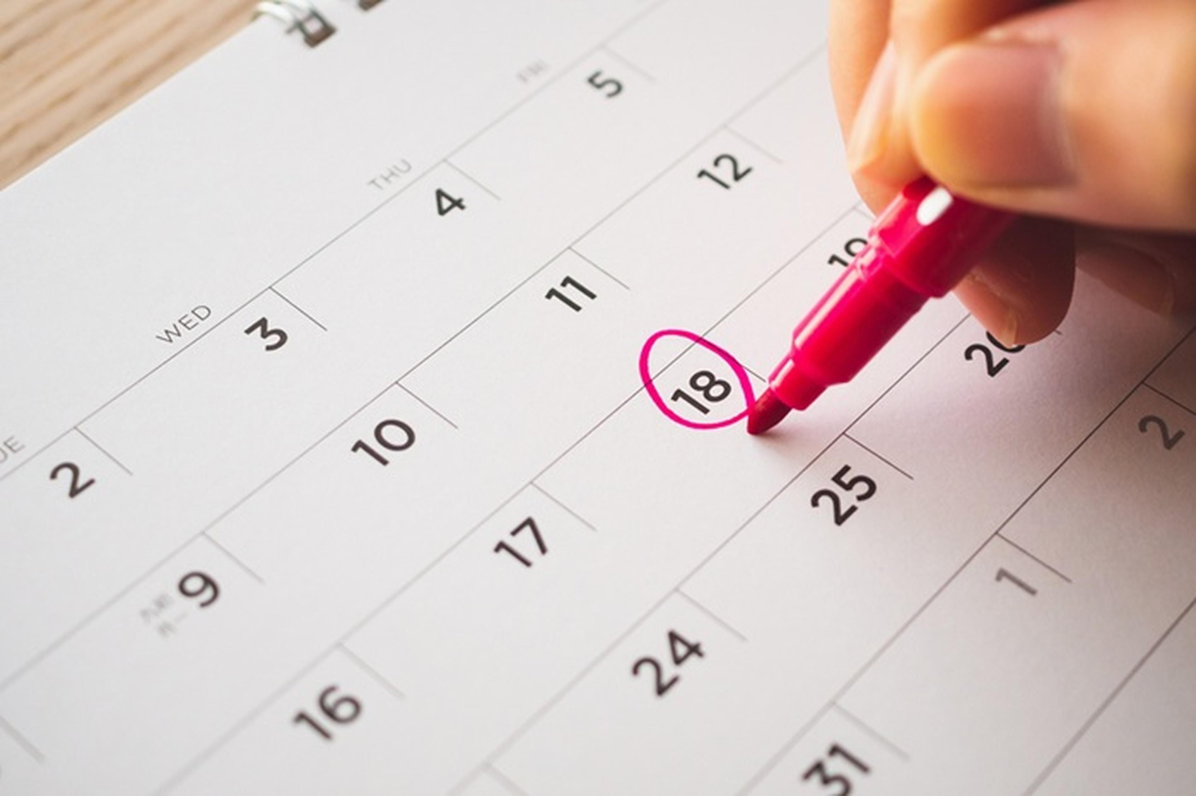 Hand holding pink marker circles the 18th on a calendar, highlighting a date on the monthly layout.