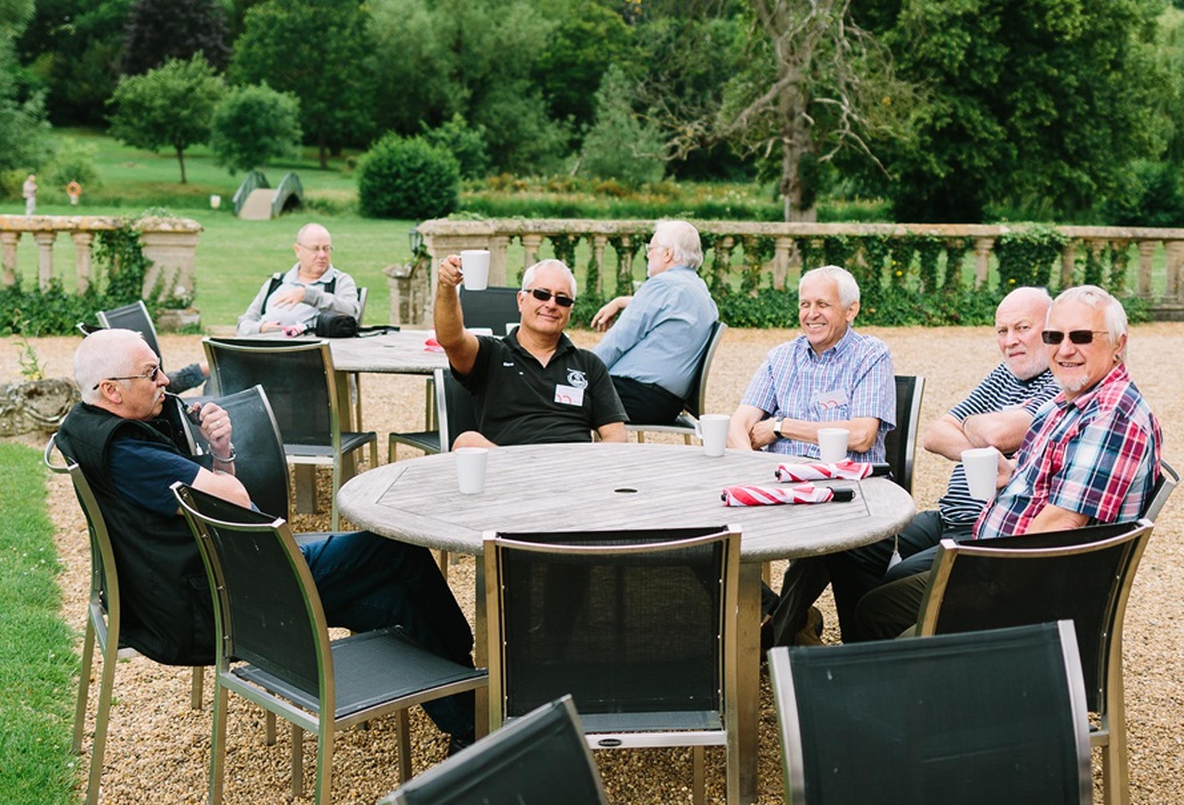 A group of Boundless members sitting outdoors around a wooden table with coffee cups
