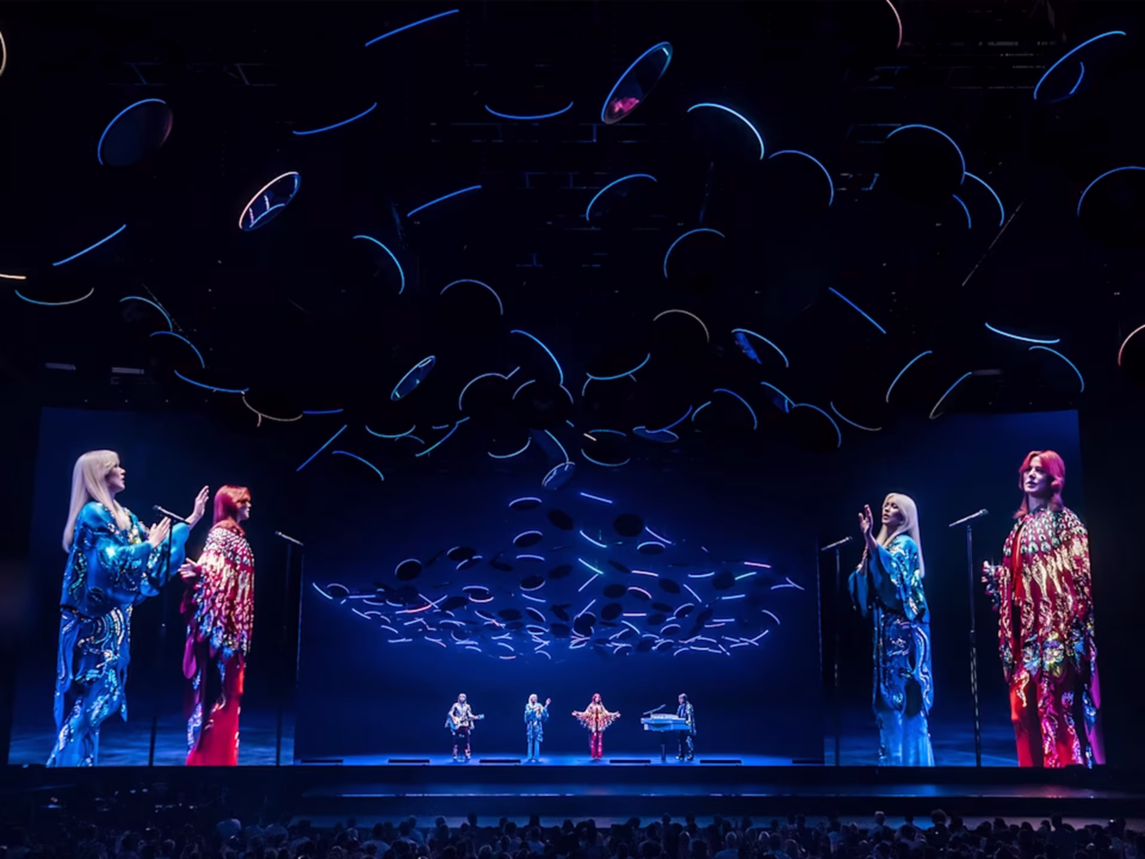 This photograph captures a vibrant moment from ABBA Voyage, with holographic avatars of the legendary pop group performing on stage in a custom-built arena The London show features elaborate visual effects, including floating hats and dynamic lighting, to recreate the music of ABBA in a fully immersive concert experience