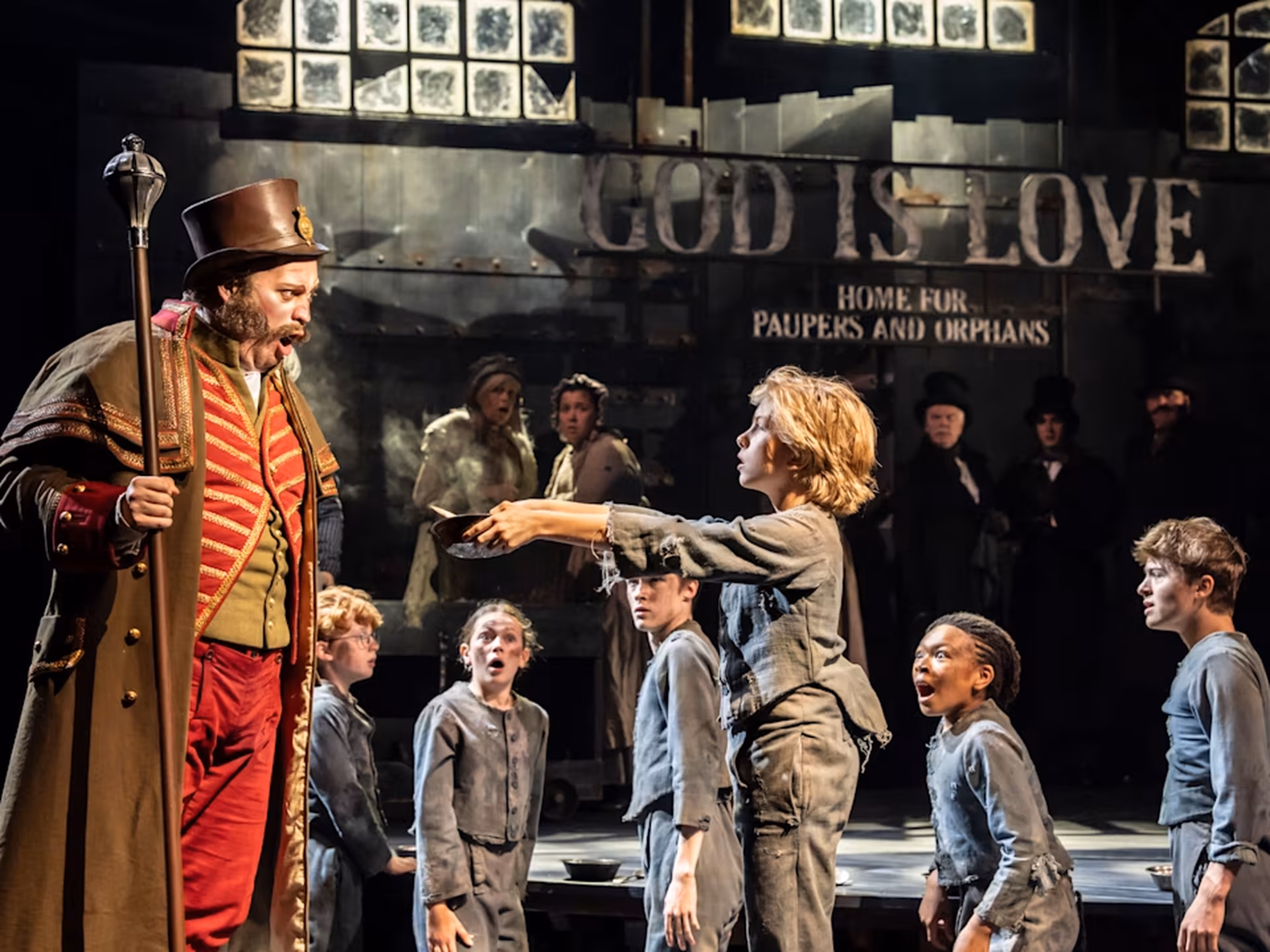 This stage photograph captures a scene from Oliver!, the West End revival of Lionel Bart’s musical adaptation of Charles Dickens’ classic novel. The production, directed by Cameron Mackintosh and choreographed by Matthew Bourne, is currently running at the Gielgud Theatre in London.