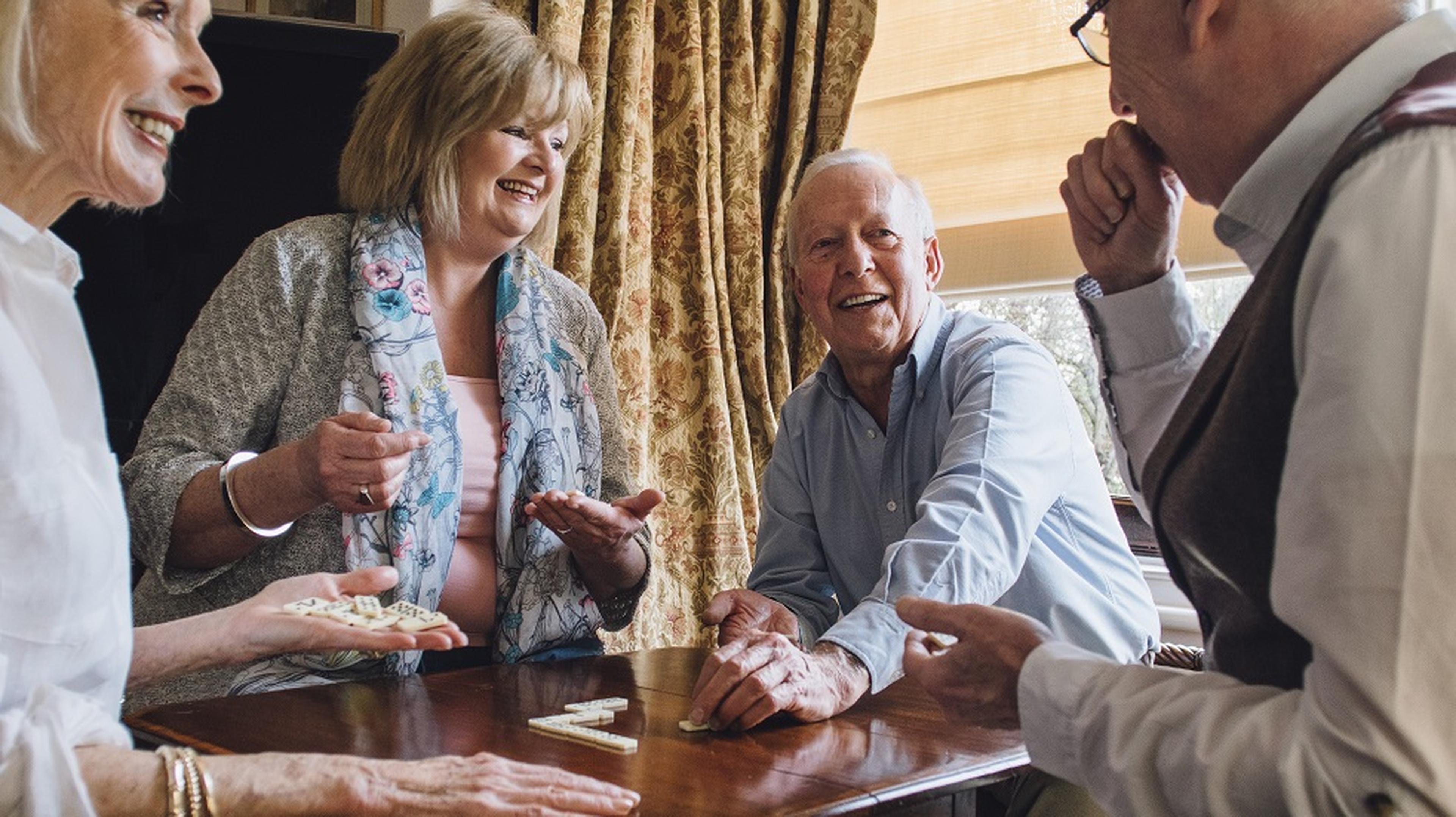 Four elderly friends enthusiastically play a board game at a wooden table