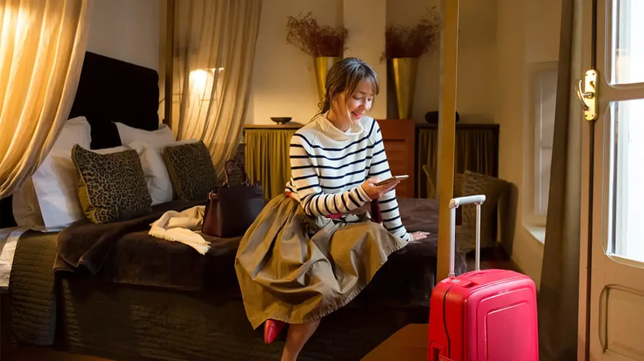 Woman sitting on a hotel bed, looking at her phone