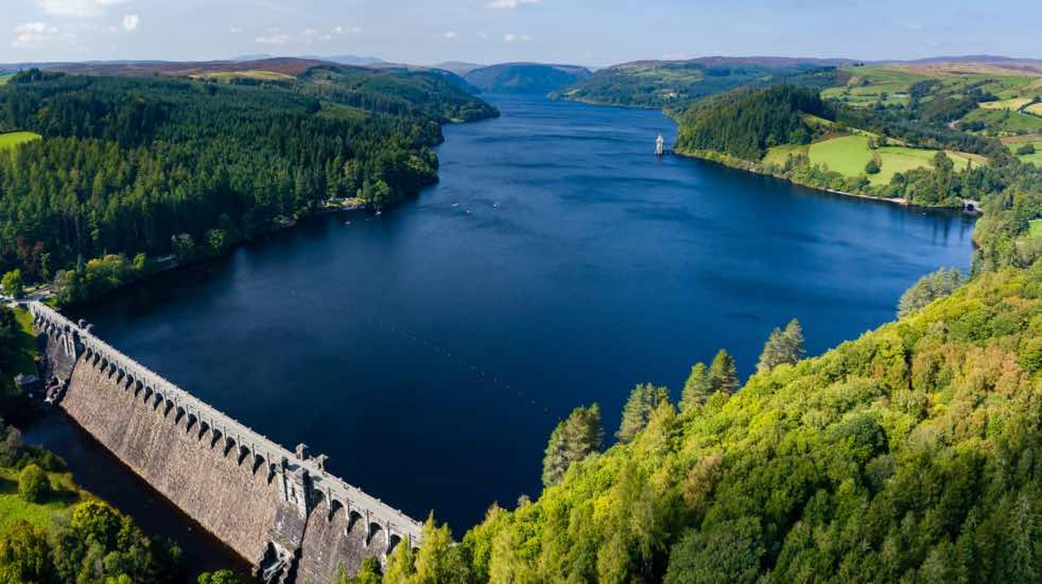 Aerial view of a dam surrounded by lush green forests and a vast blue lake