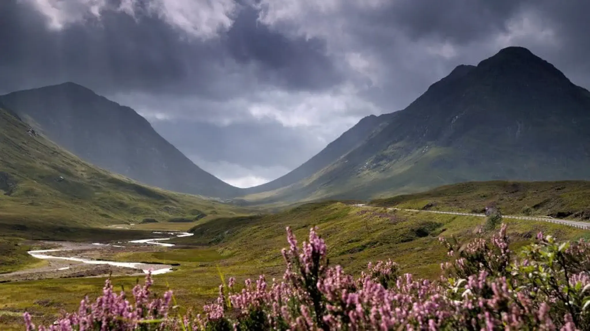 Dramatic landscape of a valley with a winding stream, green hills and dark clouds