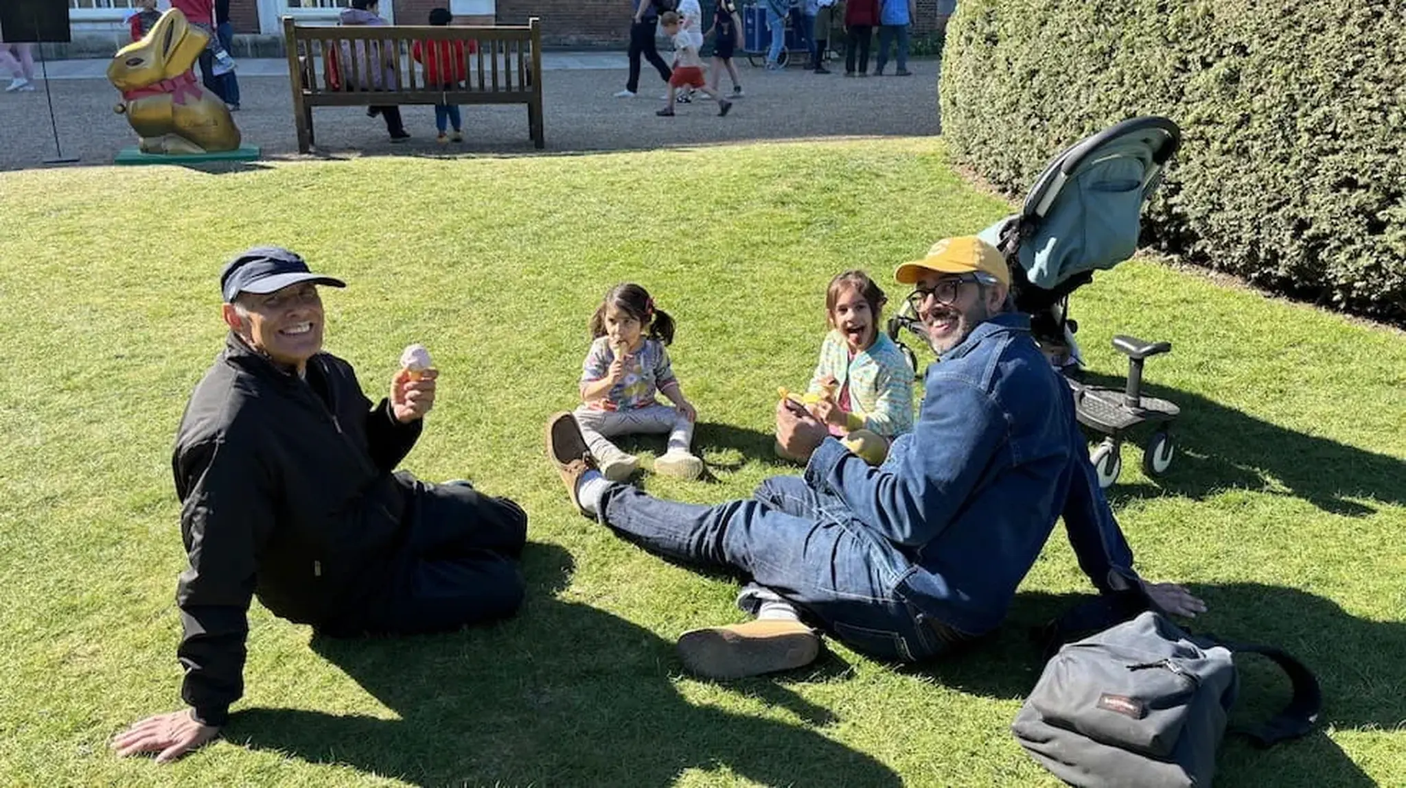 Two adults and two children sit on grass, enjoying ice cream on a sunny day
