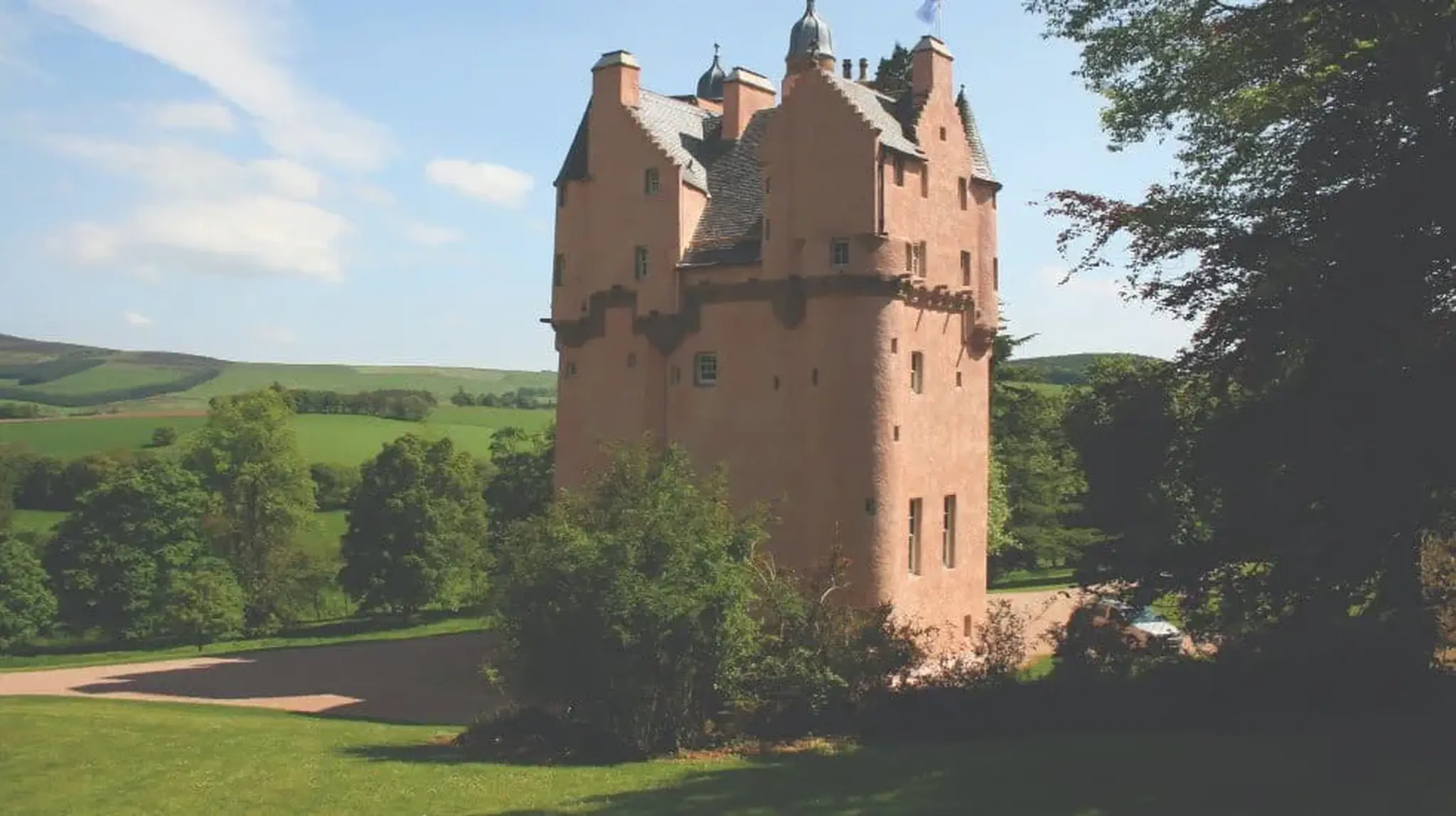 Photo of Craigievar Castle tower among green rolling hills