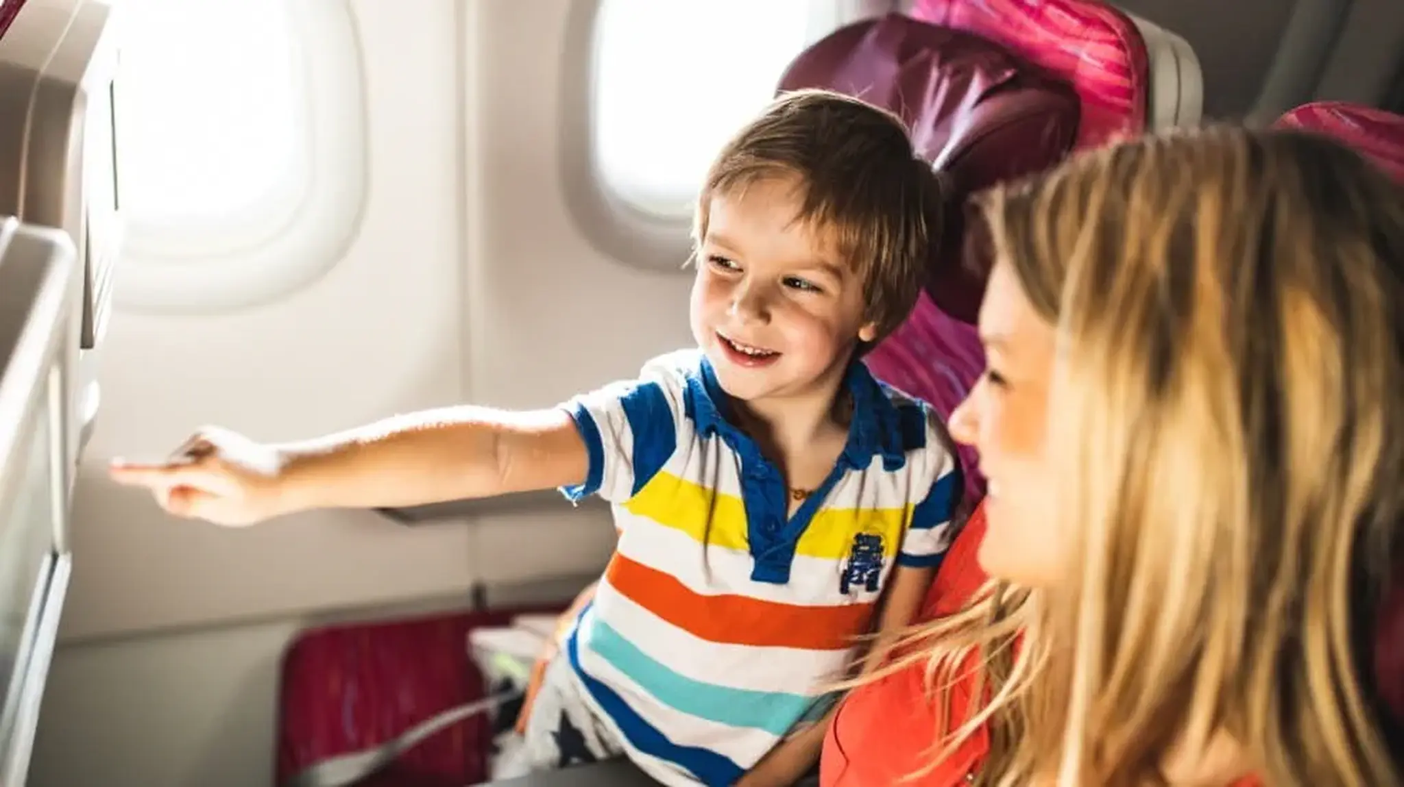 A smiling child pointing at a screen while sitting next to a woman in an airplane