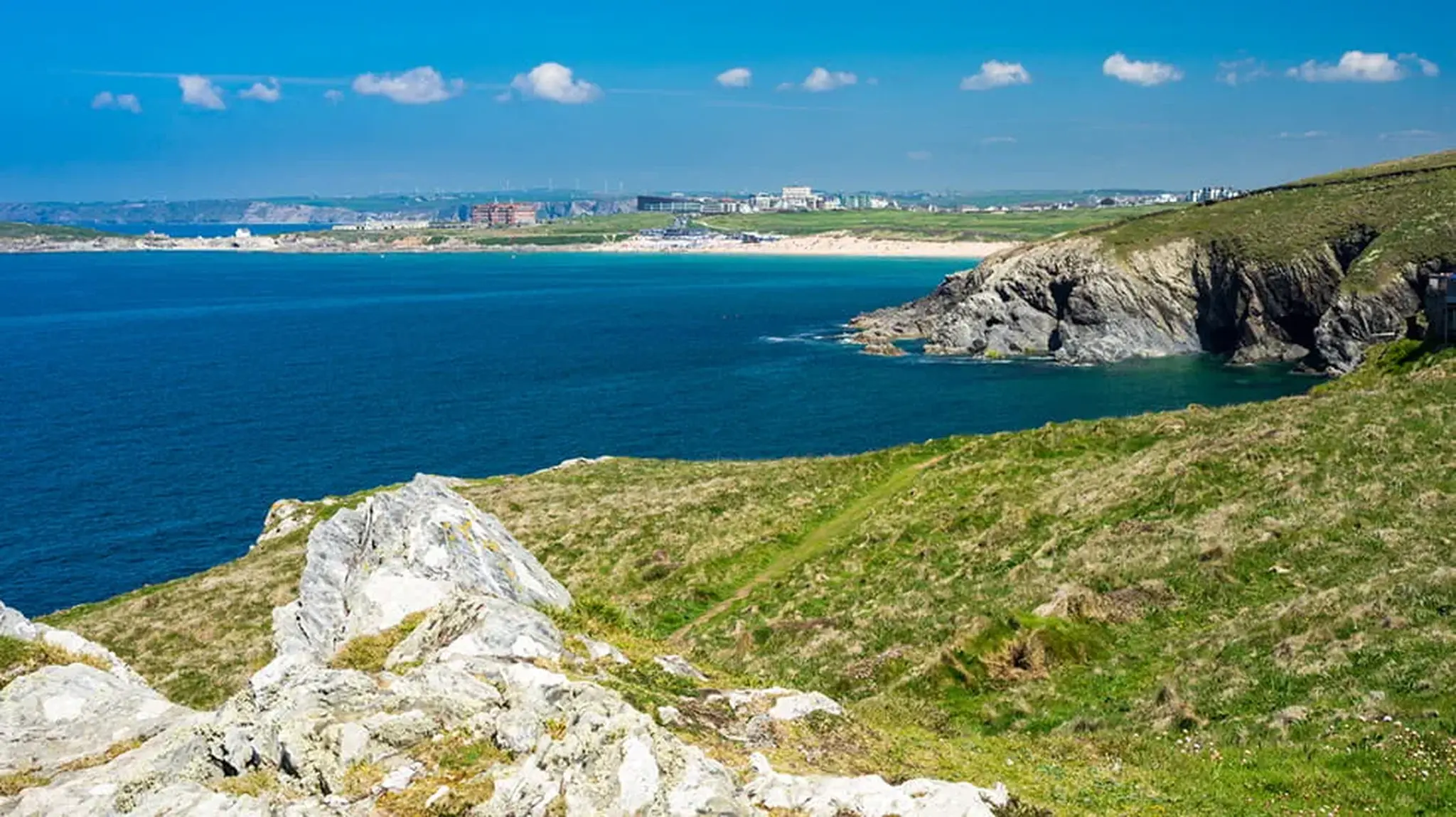 Coastal landscape with rocky cliffs, grassy foreground, and a distant sandy beach