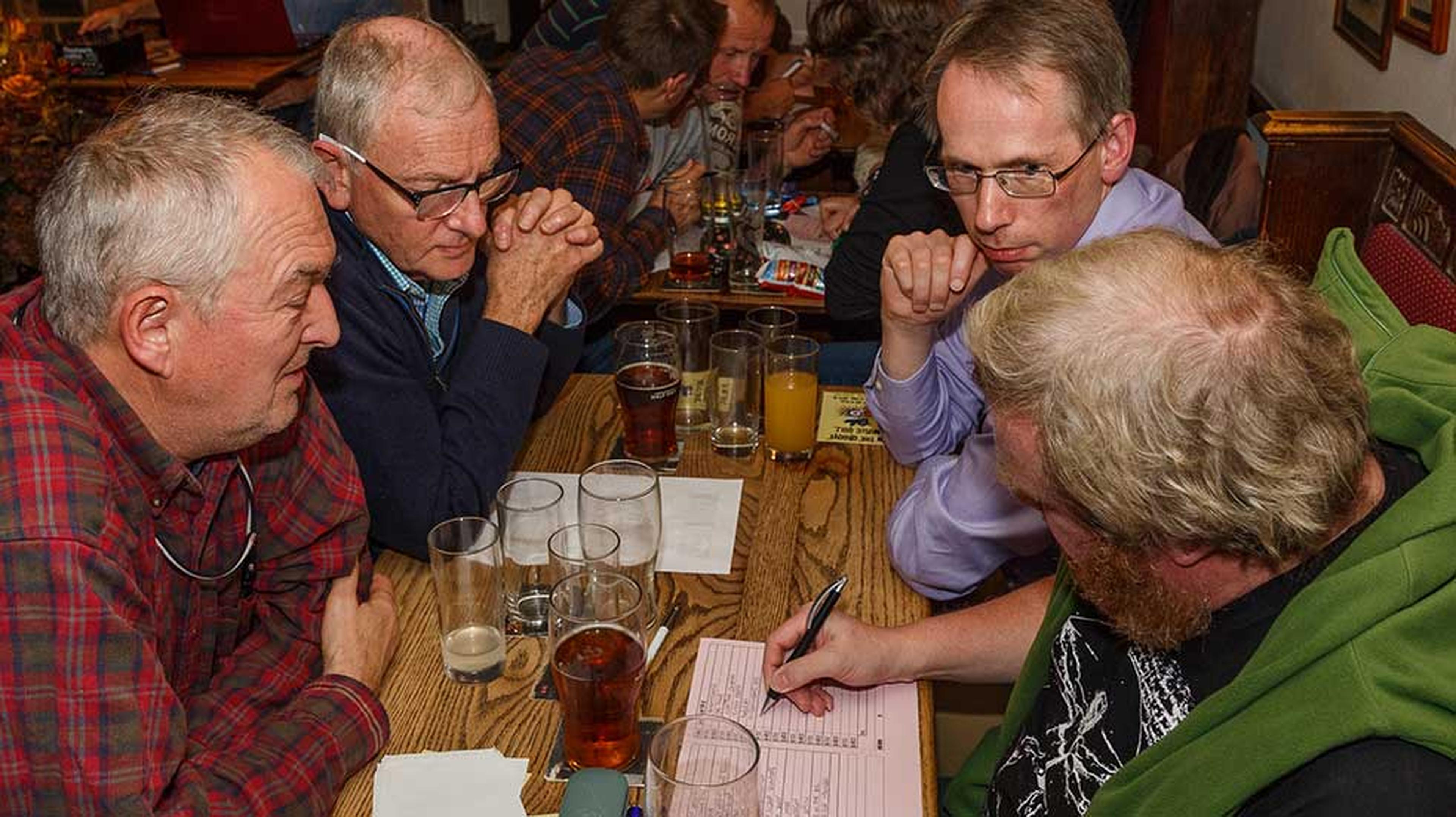 A group of four men sit around a pub table filled with drinks