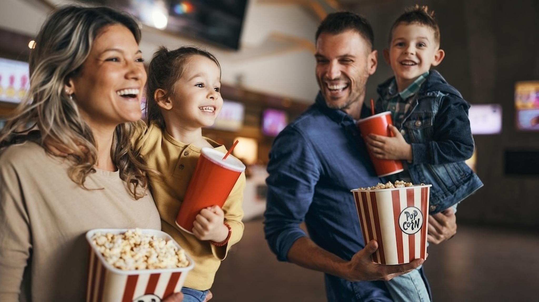 Parents and 2 children smiling holding popcorn and drinks