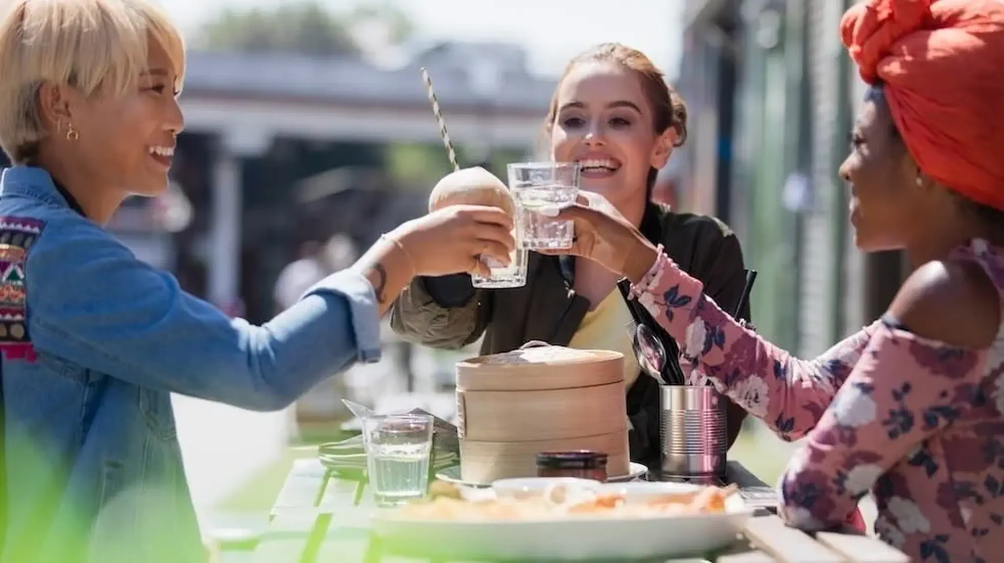 Three friends cheer with drinks at an outdoor table