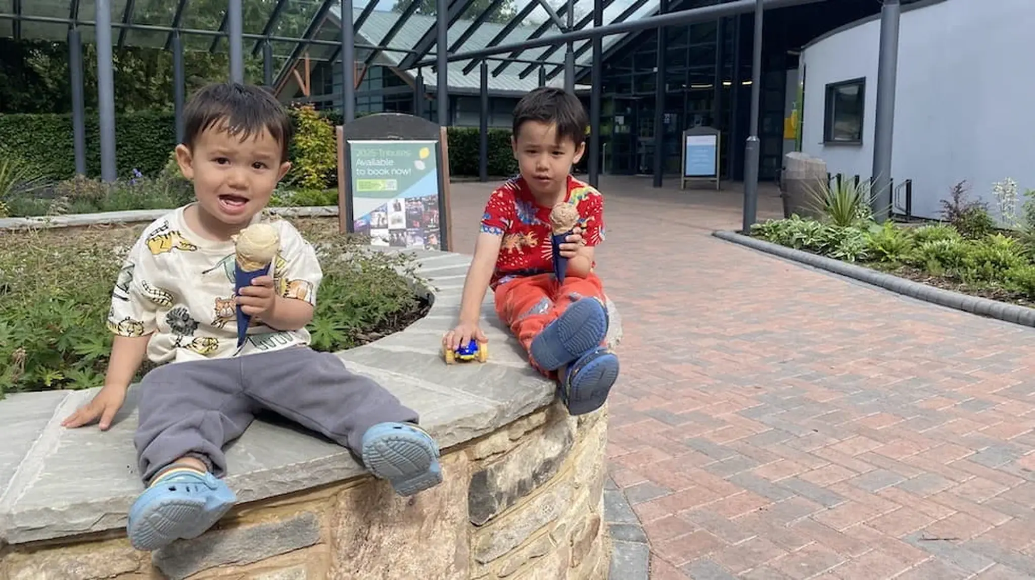 Two young boys sitting on a stone wall eating ice cream