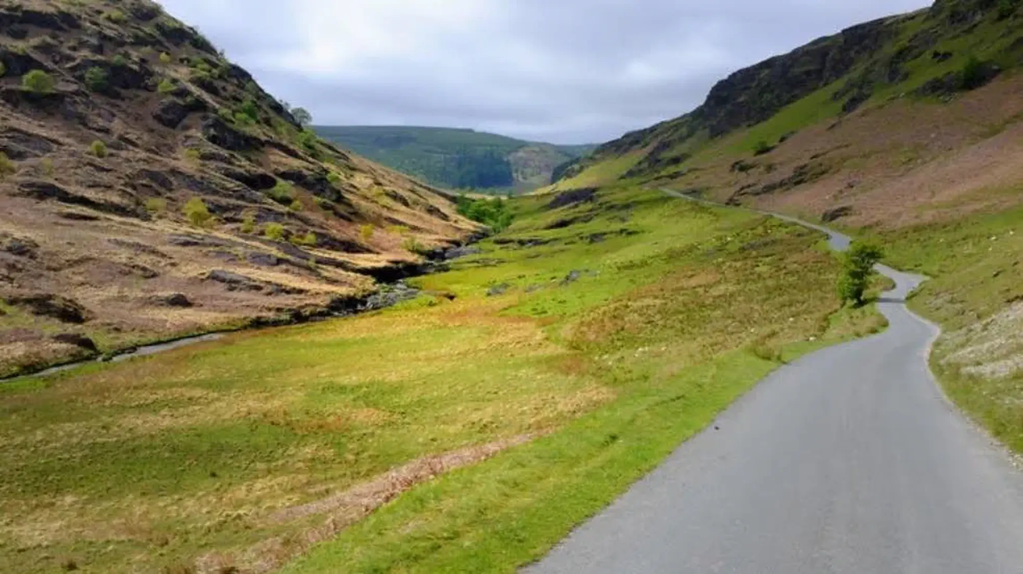 A narrow, winding road cuts through a lush, green valley with rugged hills