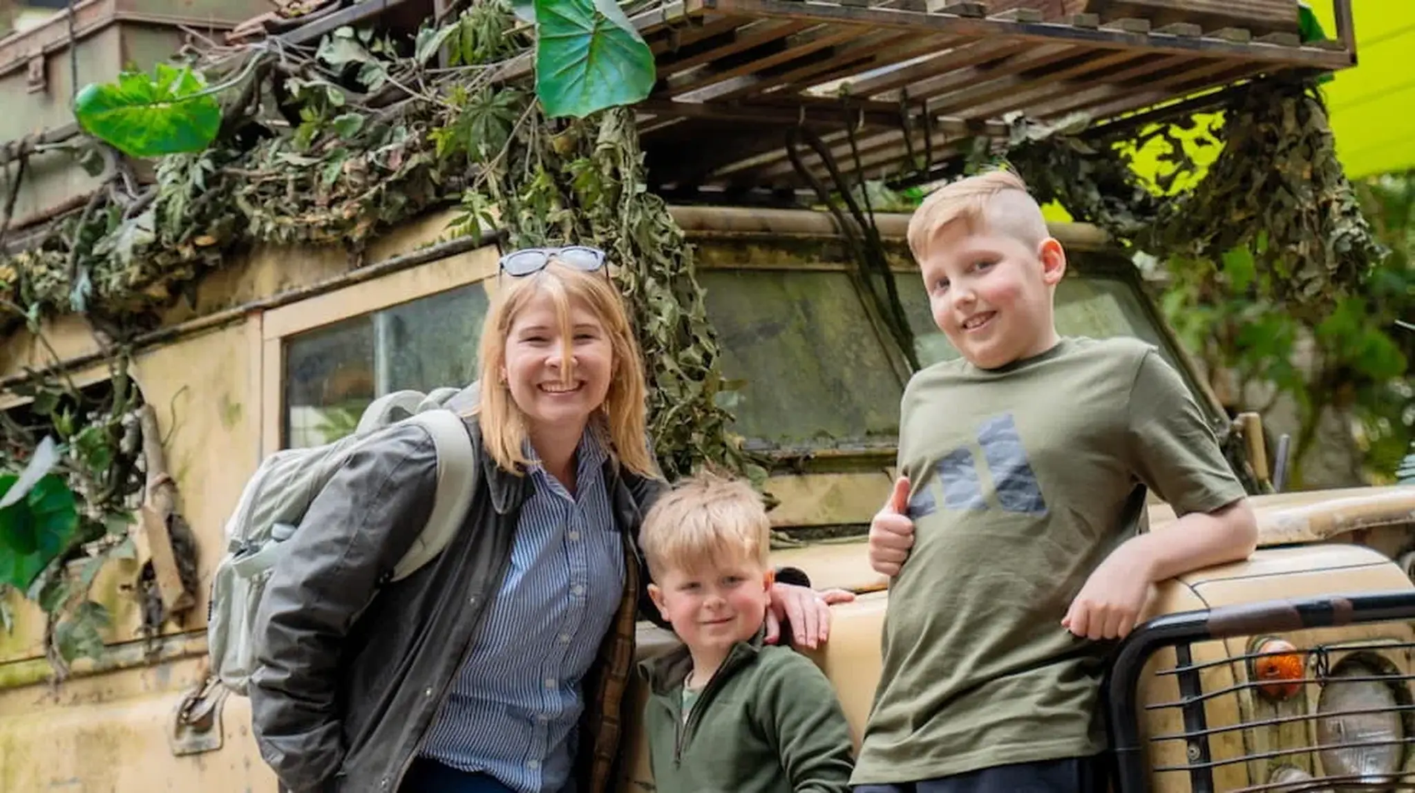 A woman and two boys smile in front of a camouflage-decorated vehicle