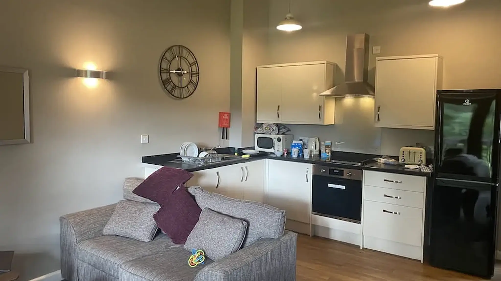 Modern kitchen and living area with a sofa, wall clock, and kitchen appliances