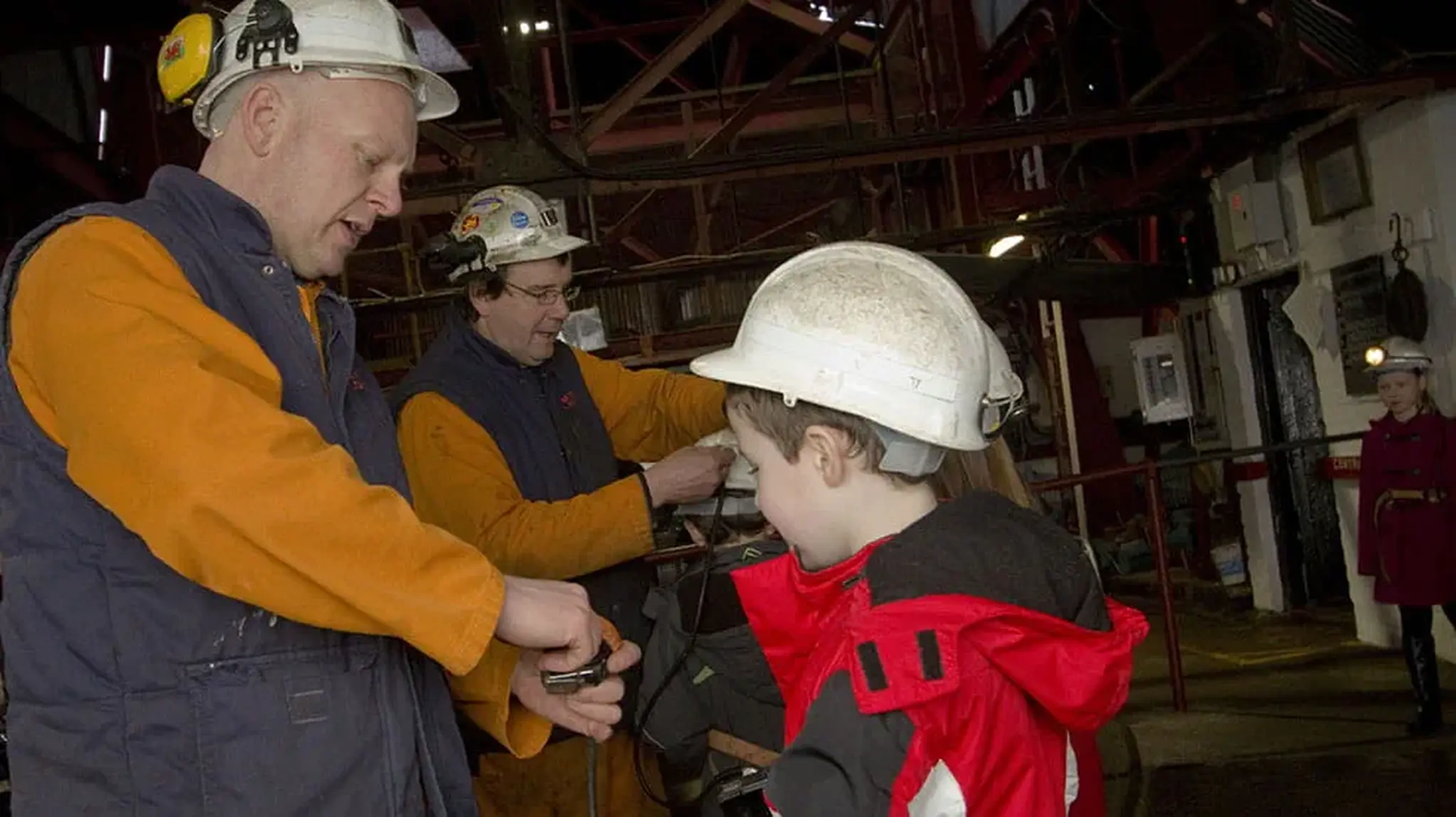 A man helps a child with safety gear in an industrial setting